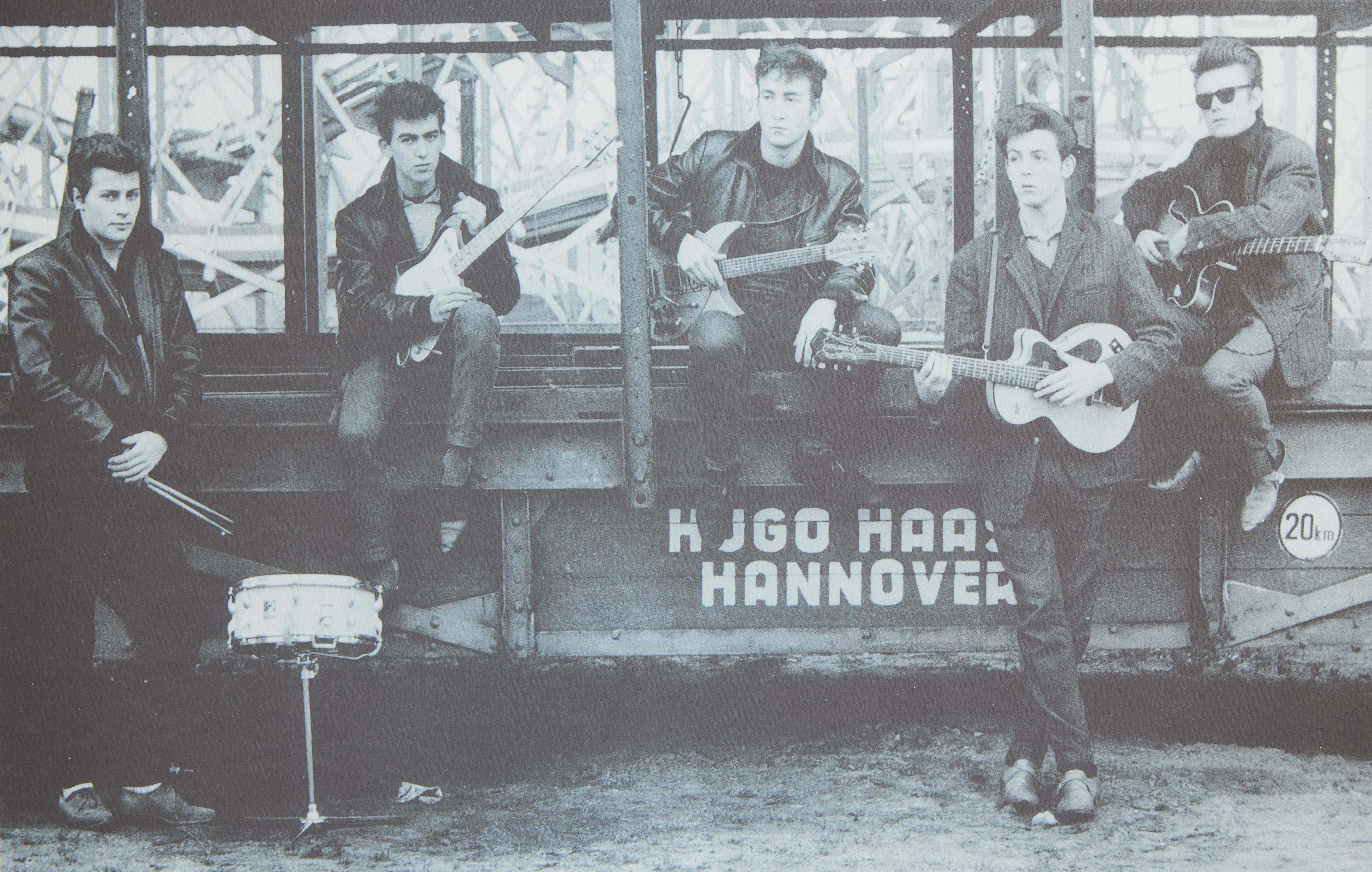 a group of young men are playing guitars and drums in a black and white photo .