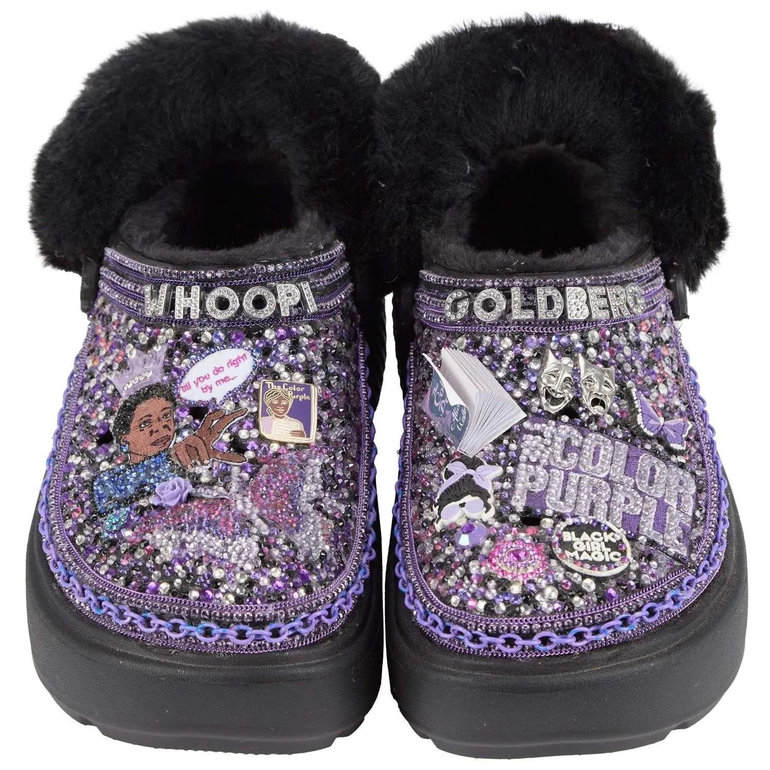 A pair of black, fur-lined clogs glitter with purple and silver rhinestones, depicting Whoopi Goldberg and elements from "The Color Purple." The left shoe says "WHOOPI" with an image of Celie, the right "GOLDBERG" and "COLOR PURPLE."