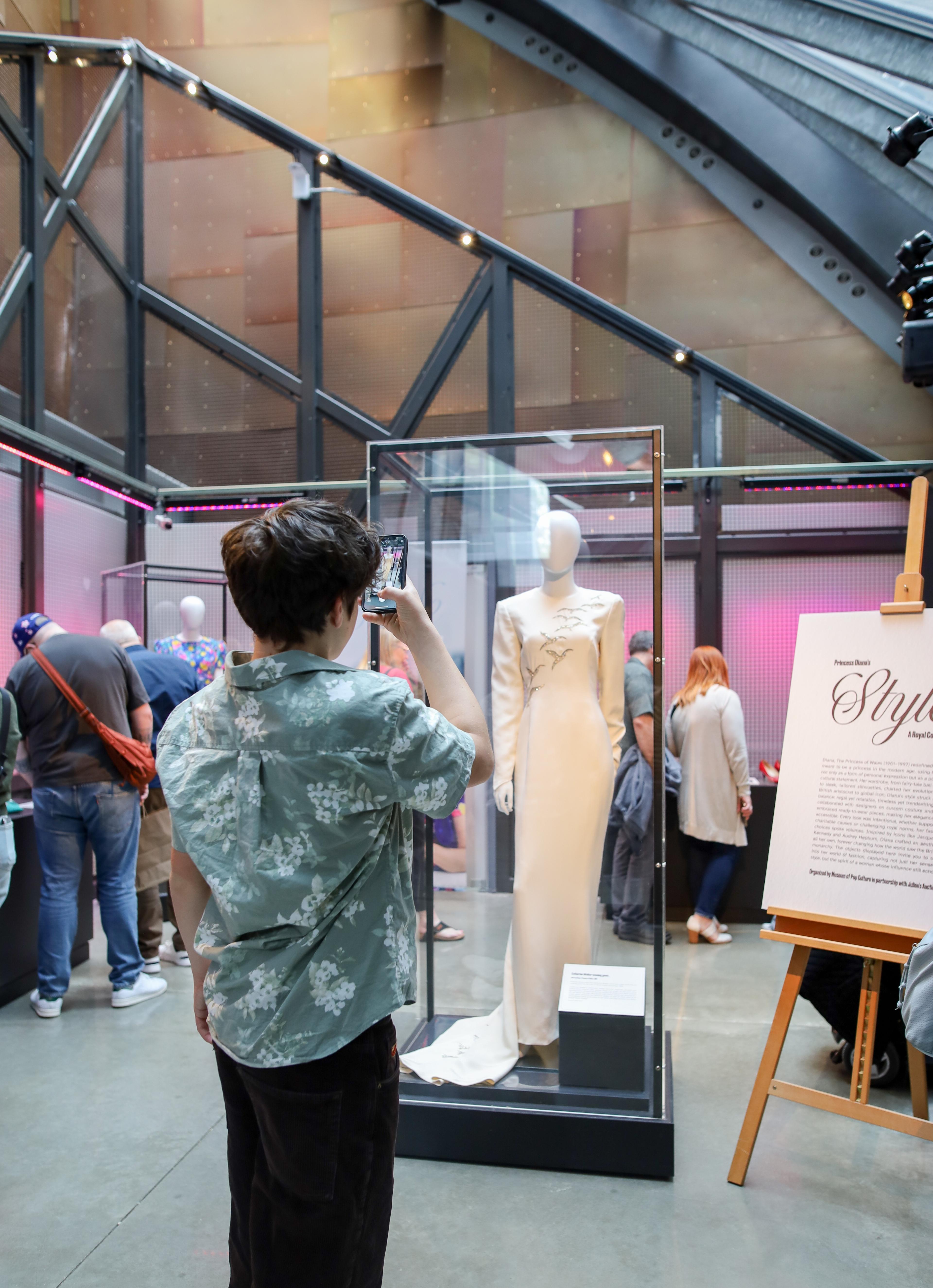 a boy takes a picture of a white dress in a display case