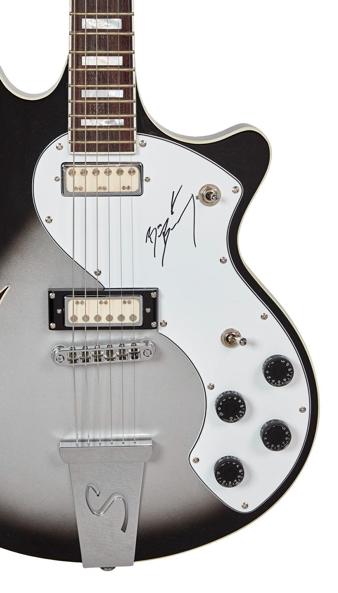 A black and silver electric guitar with a white pickguard, two cream pickups, and a signature in black ink on the pickguard.