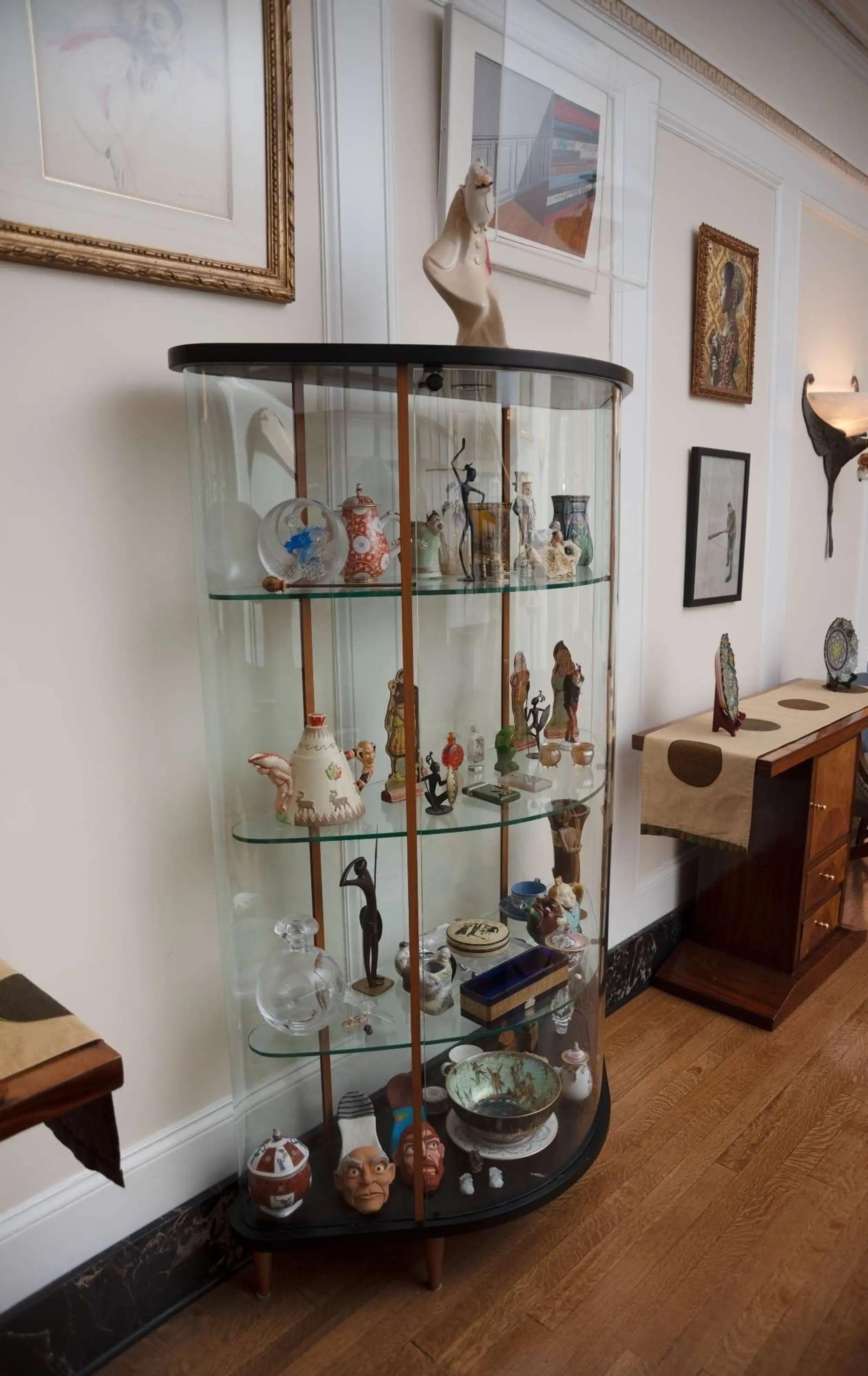 A tall, curved glass display cabinet filled with diverse figurines, masks, and decorative objects.