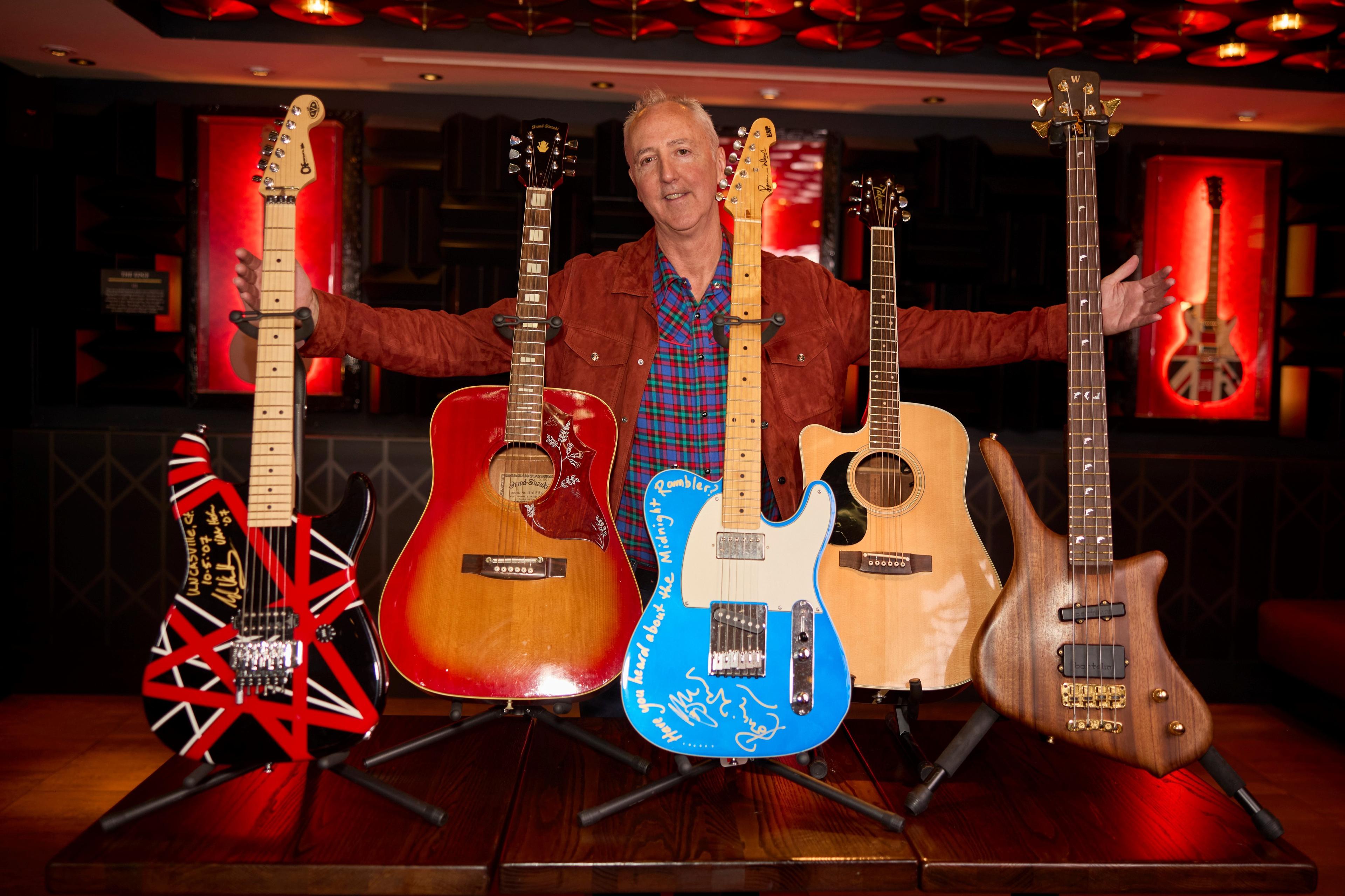 a man standing behind five guitars on display