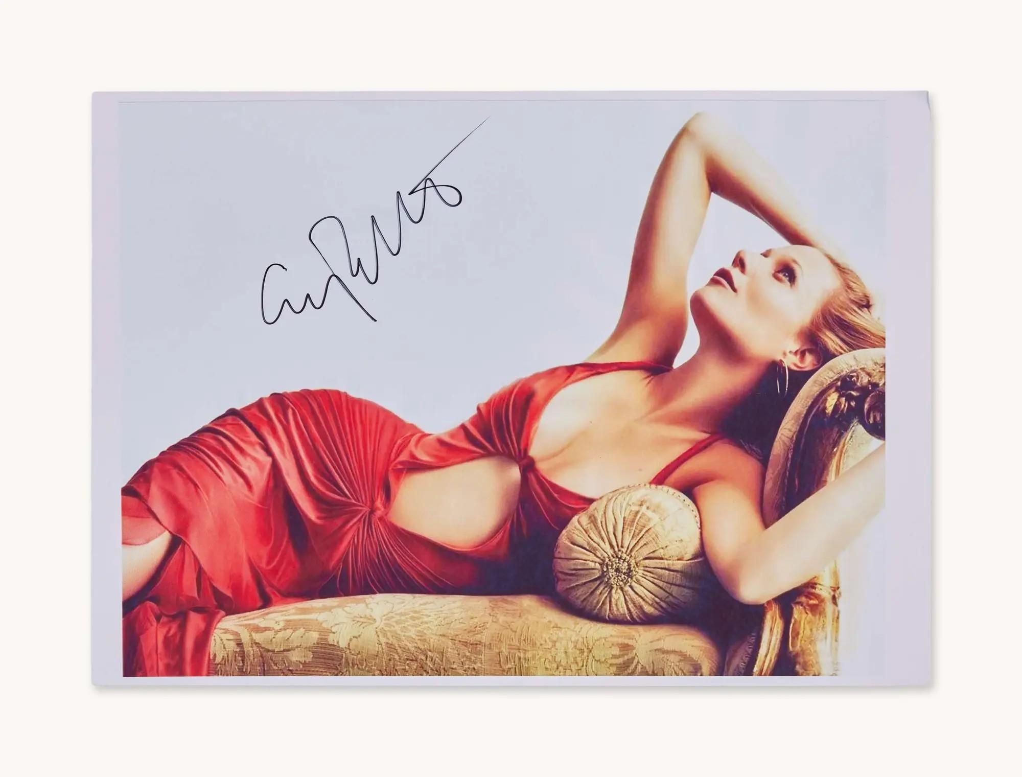a signed photo of Gwyneth Paltrow wearing a red dress while laying on a gold chaise sofa