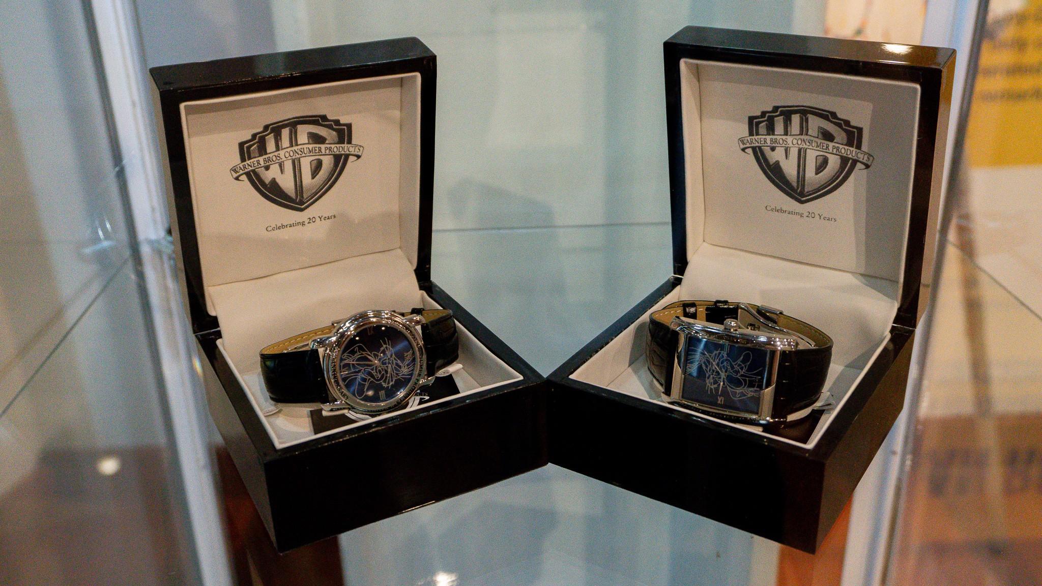 two watches are in wooden boxes on a glass shelf .