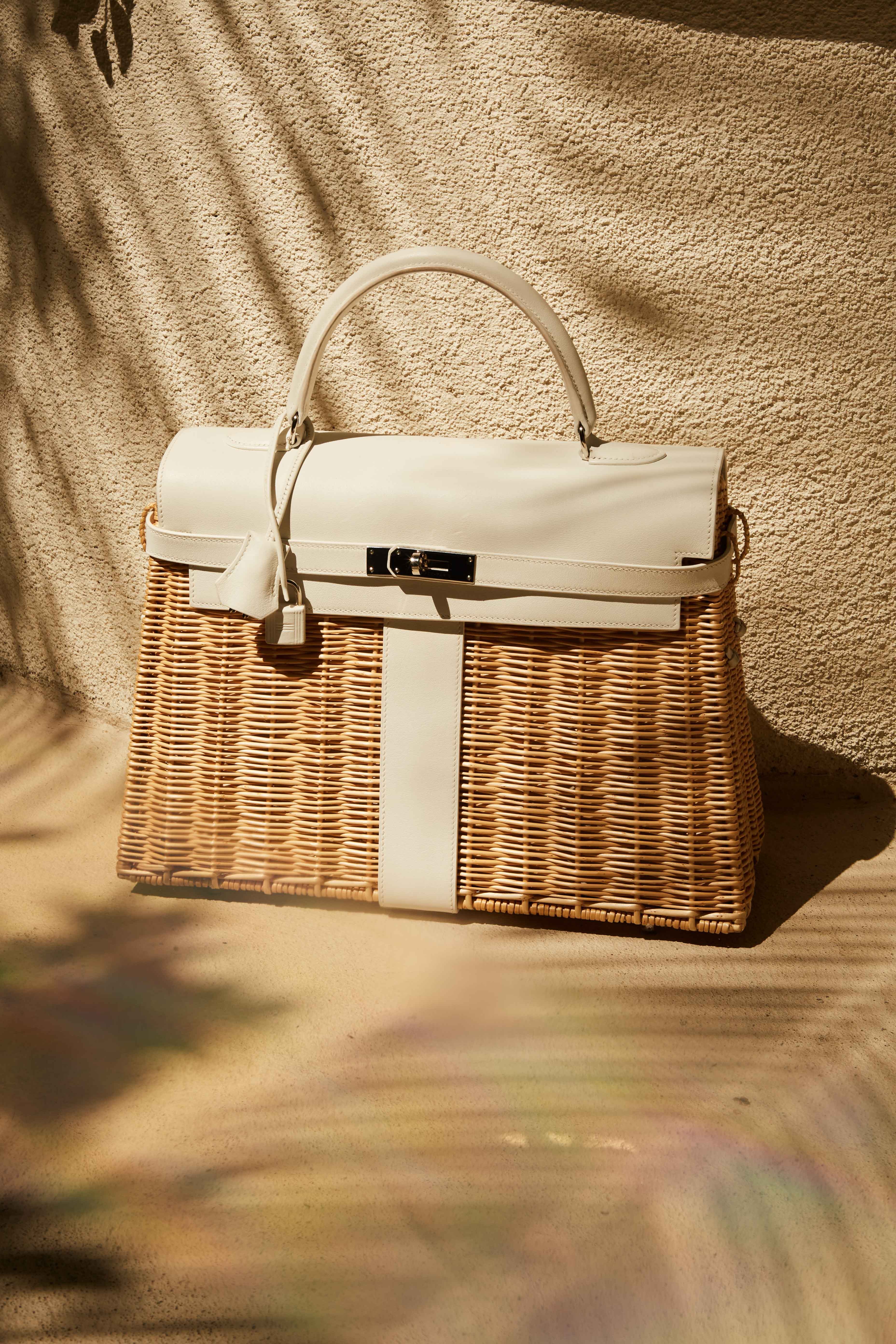 Lot 5, Hermes Wicker Kelly a wicker bag with a white handle is sitting on a sandy surface .