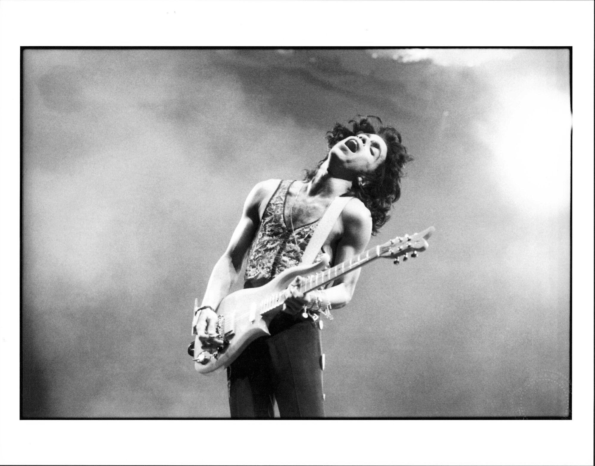 a black and white photo of prince playing a guitar on stage .
