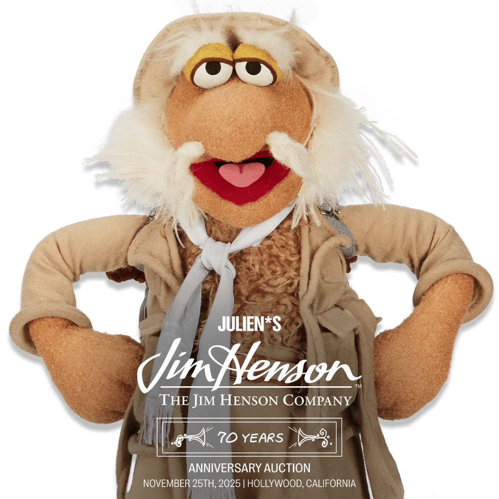 A friendly, white-bearded Jim Henson puppet wearing a tan explorer hat, advertising 'Julien's Jim Henson 70 Years Anniversary Auction, November 25th, 2025'.