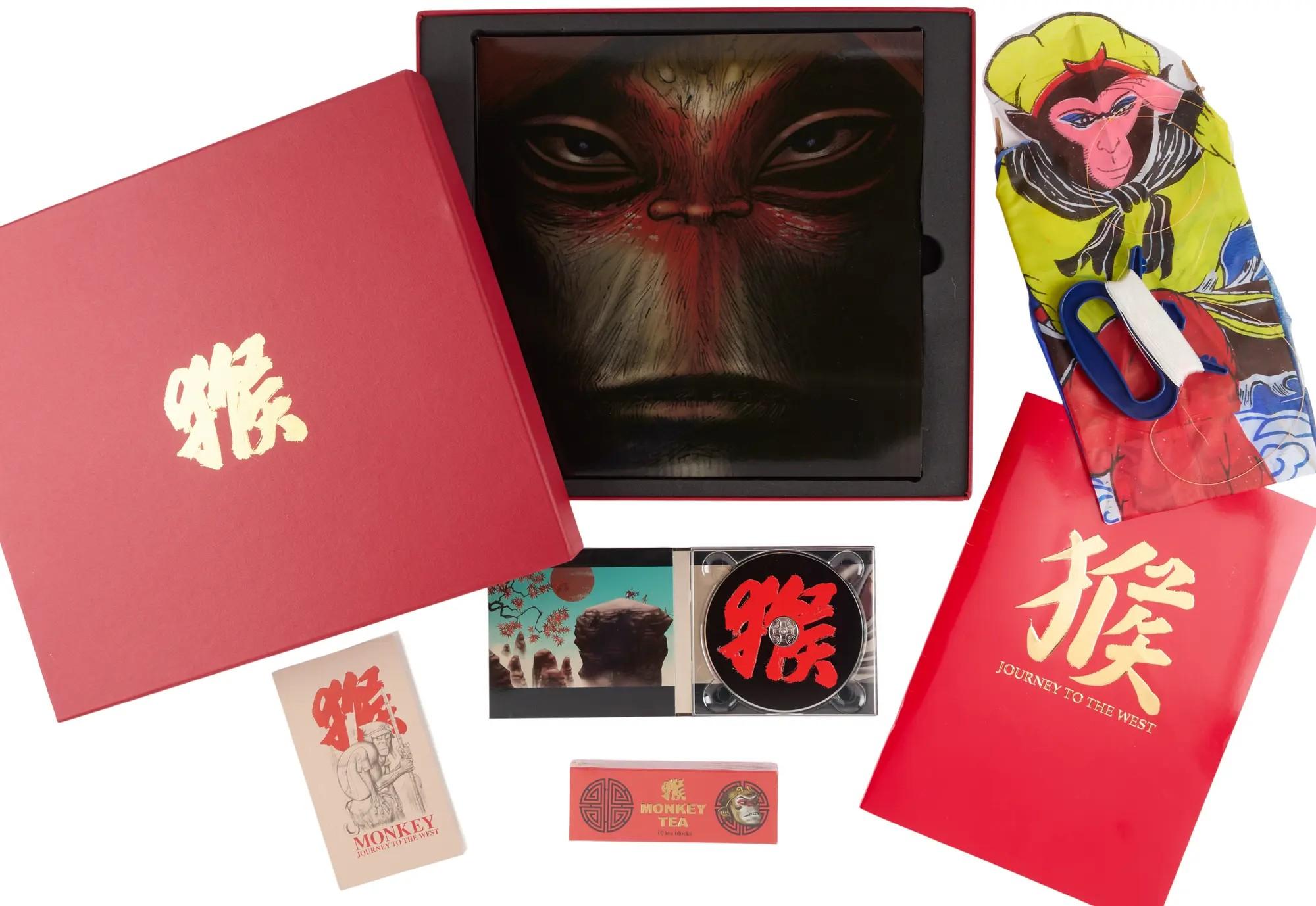 Collection of "Monkey: Journey to the West" merchandise, including a red presentation box with monkey artwork, a CD, a patterned scarf, booklets, and "Monkey Tea."