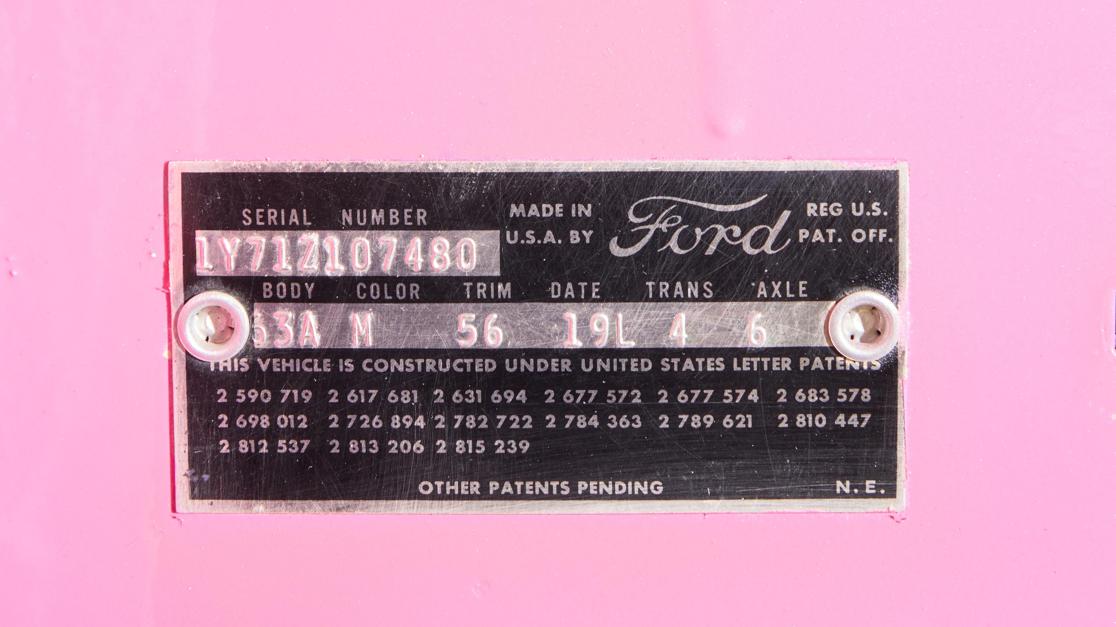A black Ford data plate with white text on a pink background, showing a serial number and other vehicle specifications.