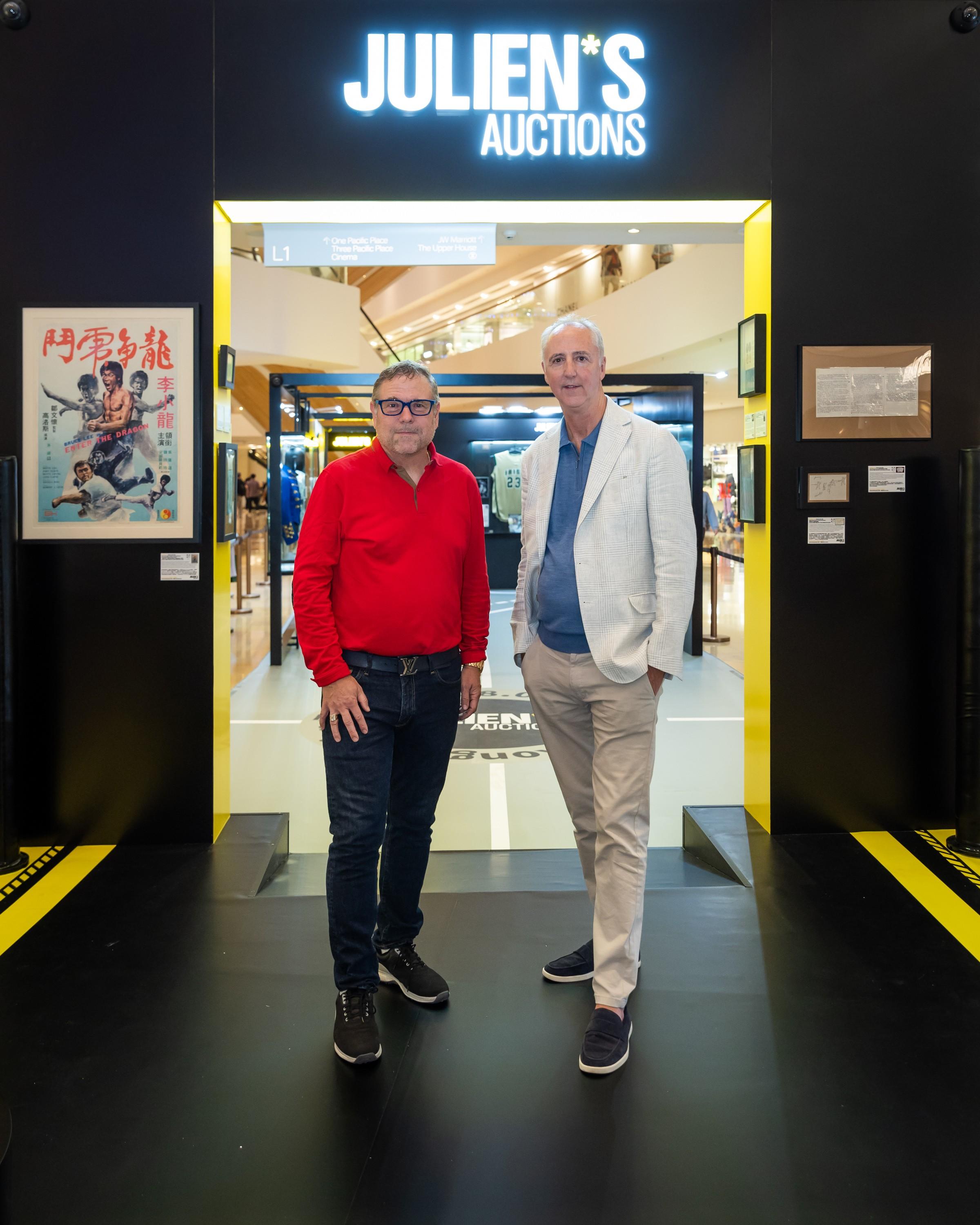 two men stand in front of a julien 's auctions sign