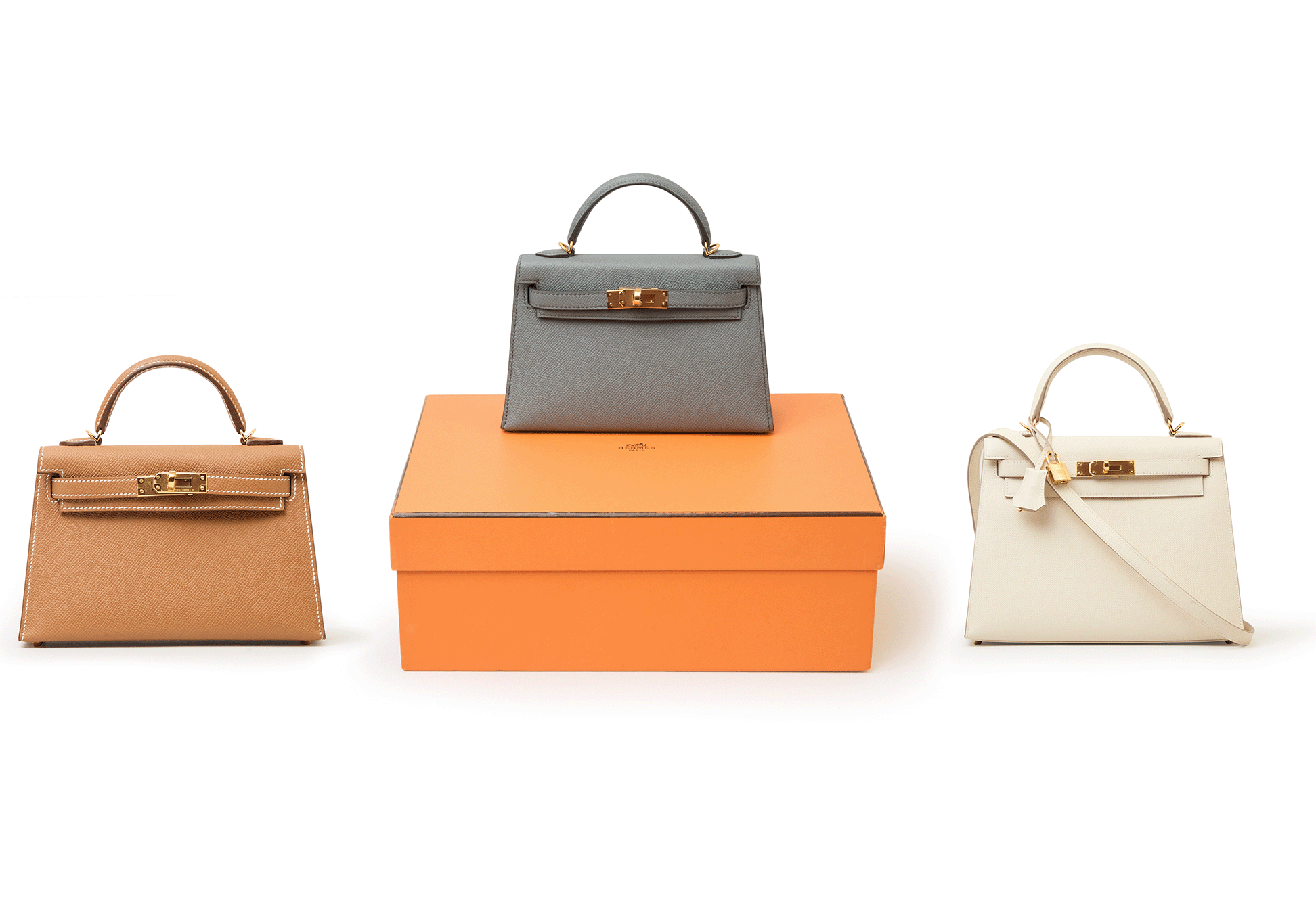 a brown hermes handbag with a gray hermes handbag resting on an orange box beside a white hermes handbag