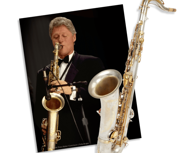 Bill Clinton playing a saxophone in a tuxedo, next to another saxophone.