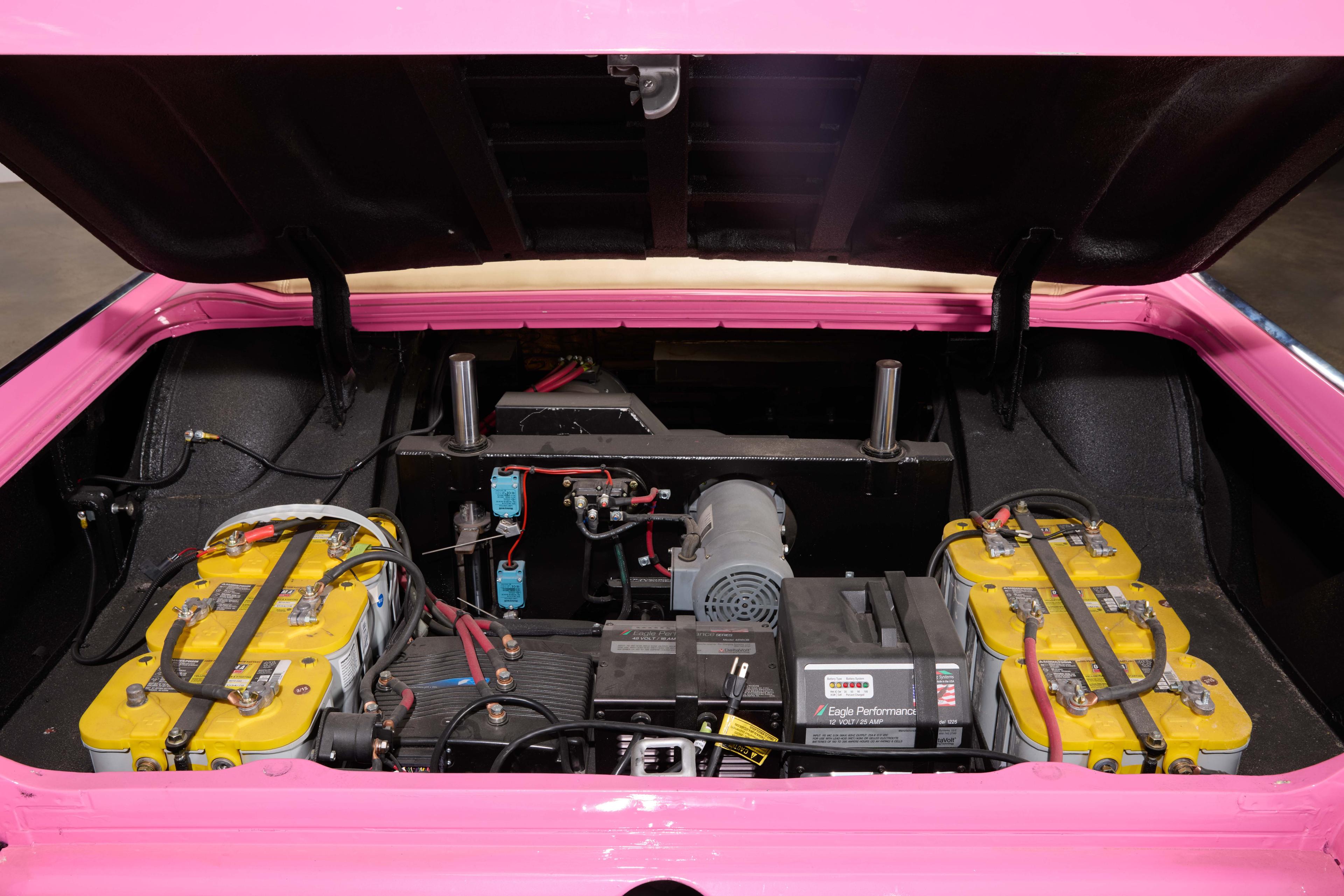 Open trunk of a pink car showing an electric motor and multiple yellow batteries.