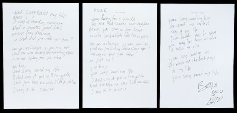 Three white sheets of paper with handwritten lyrics, the rightmost signed "Bono."