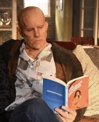 a bald man is sitting on a couch reading a book .