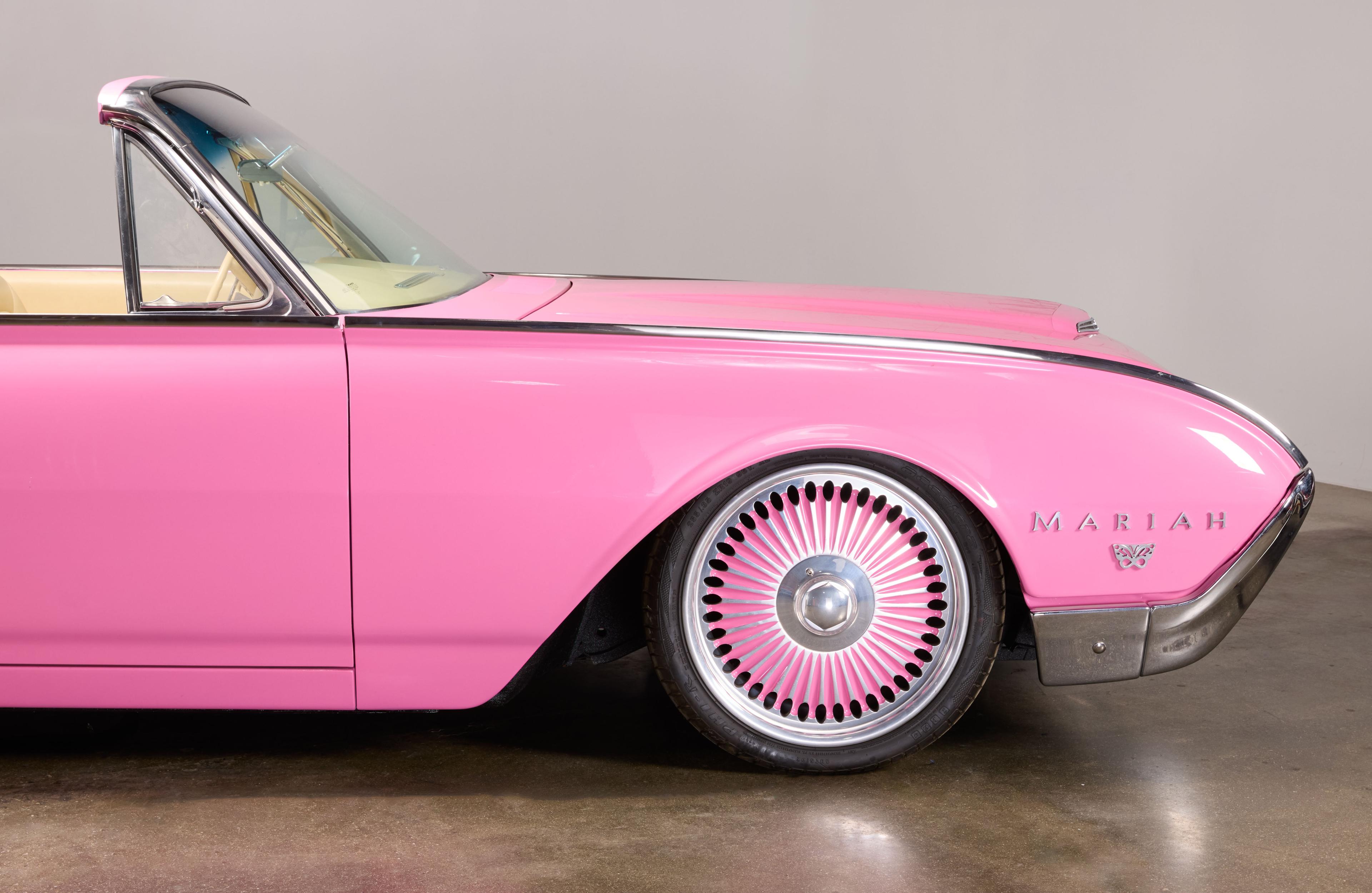 Side view of a pink vintage convertible car with "MARIAH" on the fender and custom pink and silver wheels.