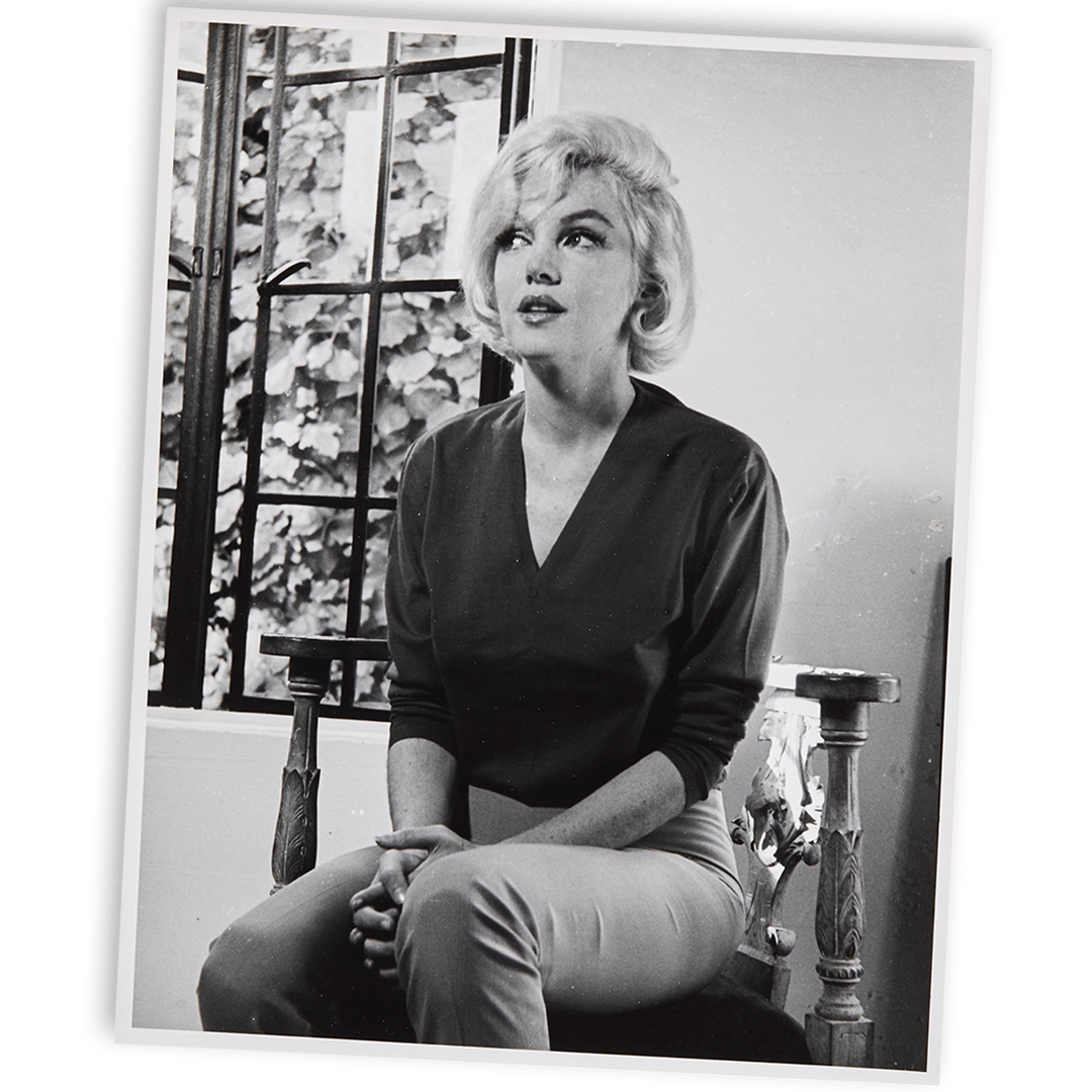Black and white photo of Marilyn Monroe seated, looking upward.