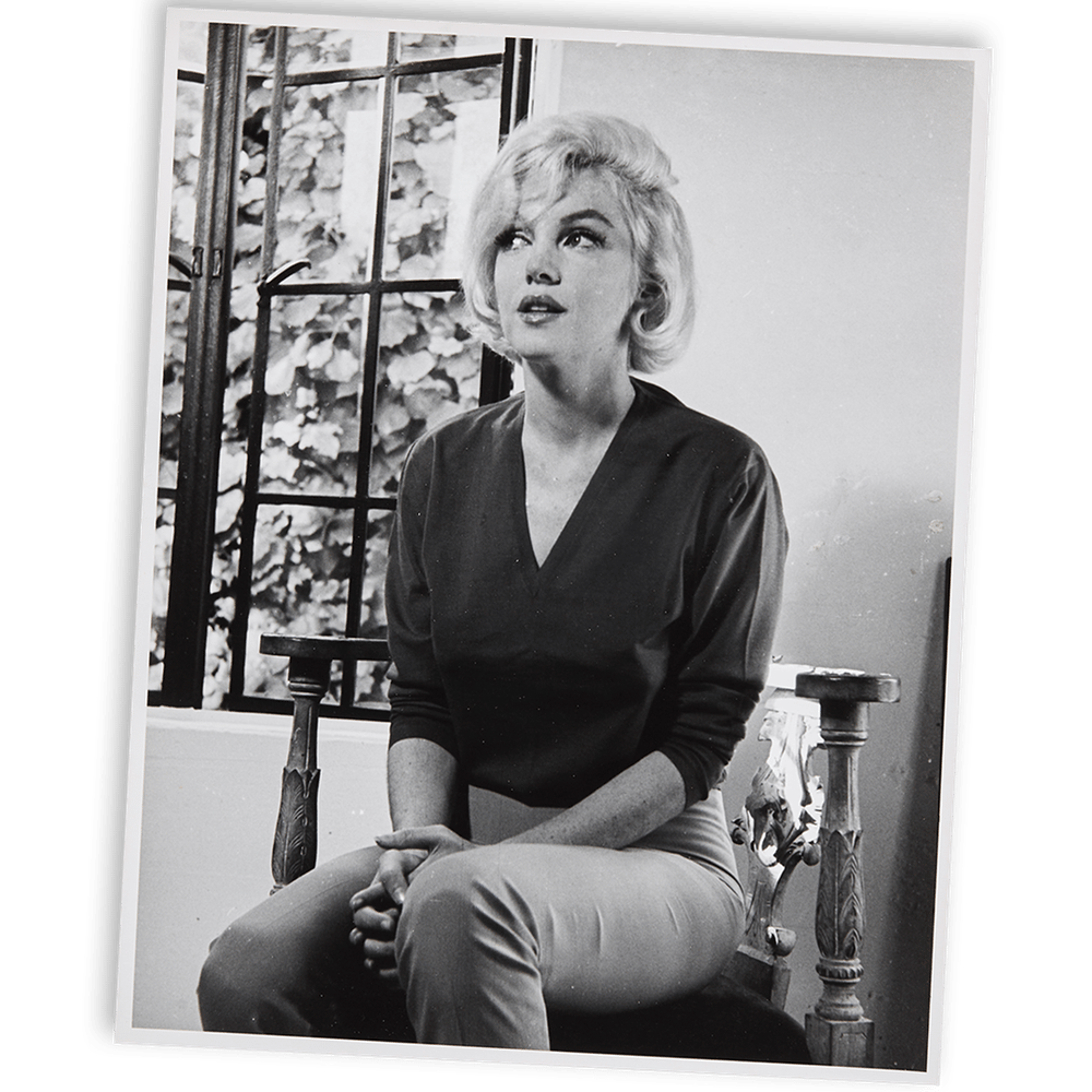 Black and white photo of Marilyn Monroe seated, looking upward.