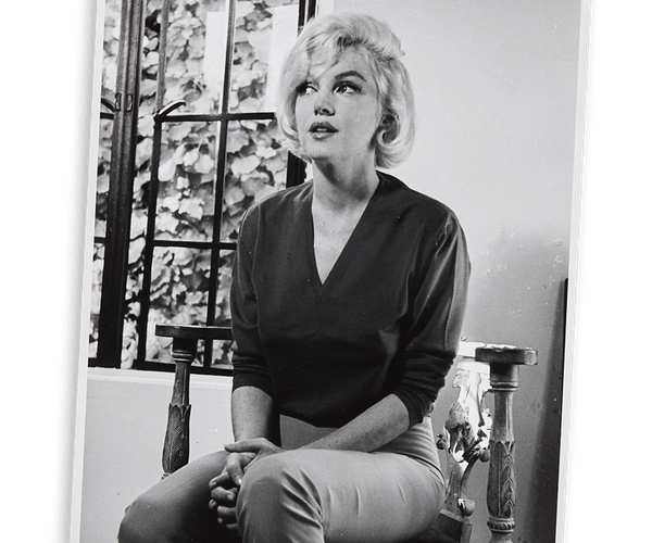 Black and white photo of Marilyn Monroe seated, looking upward.