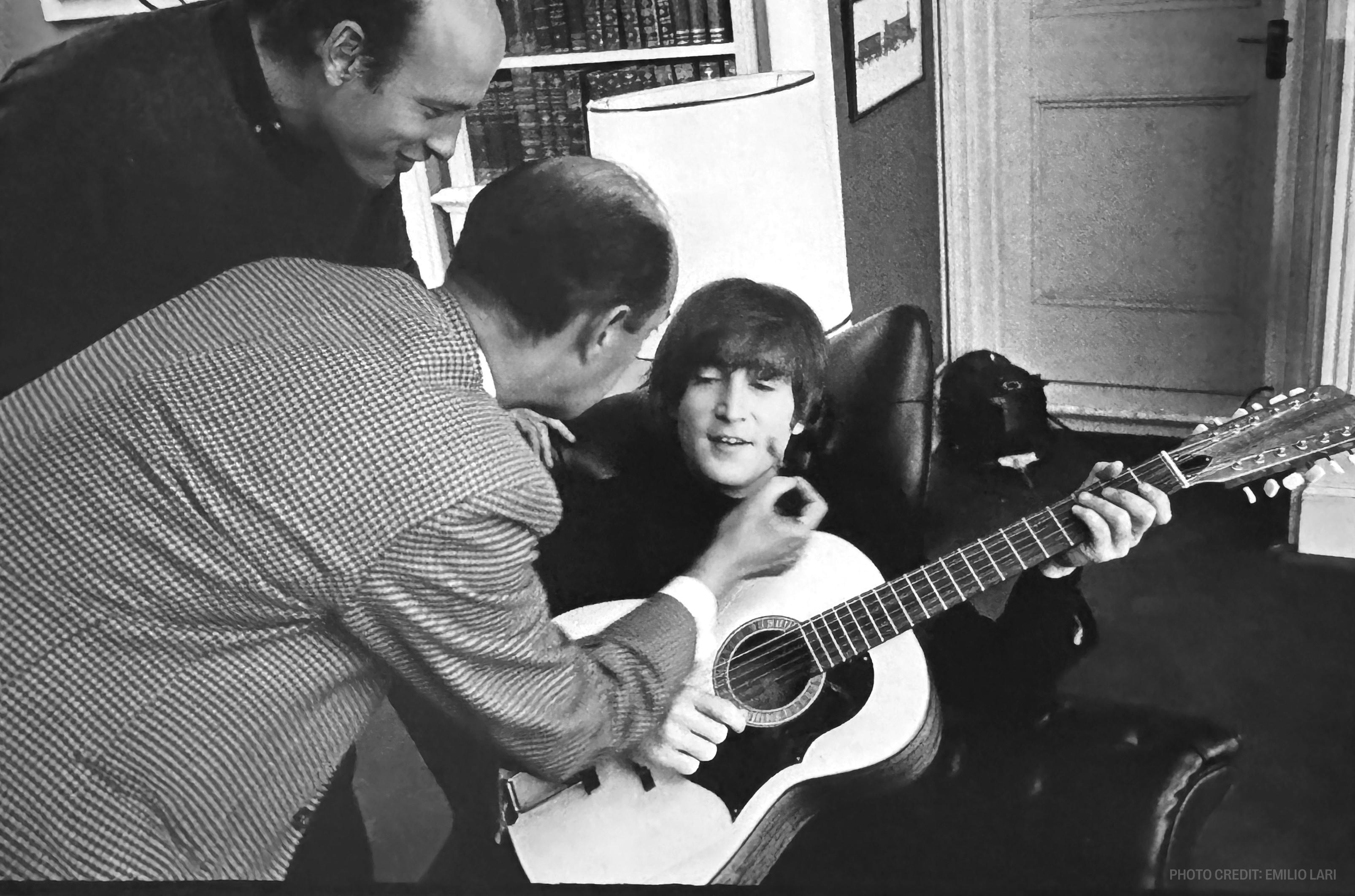 a man is helping a young boy play a guitar in a black and white photo .