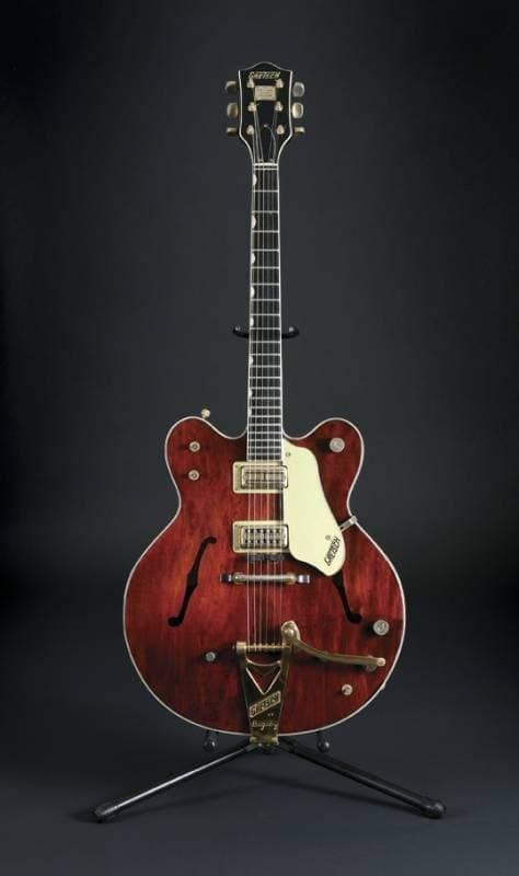 A cherry red Gretsch hollow-body electric guitar with f-holes, on a stand.