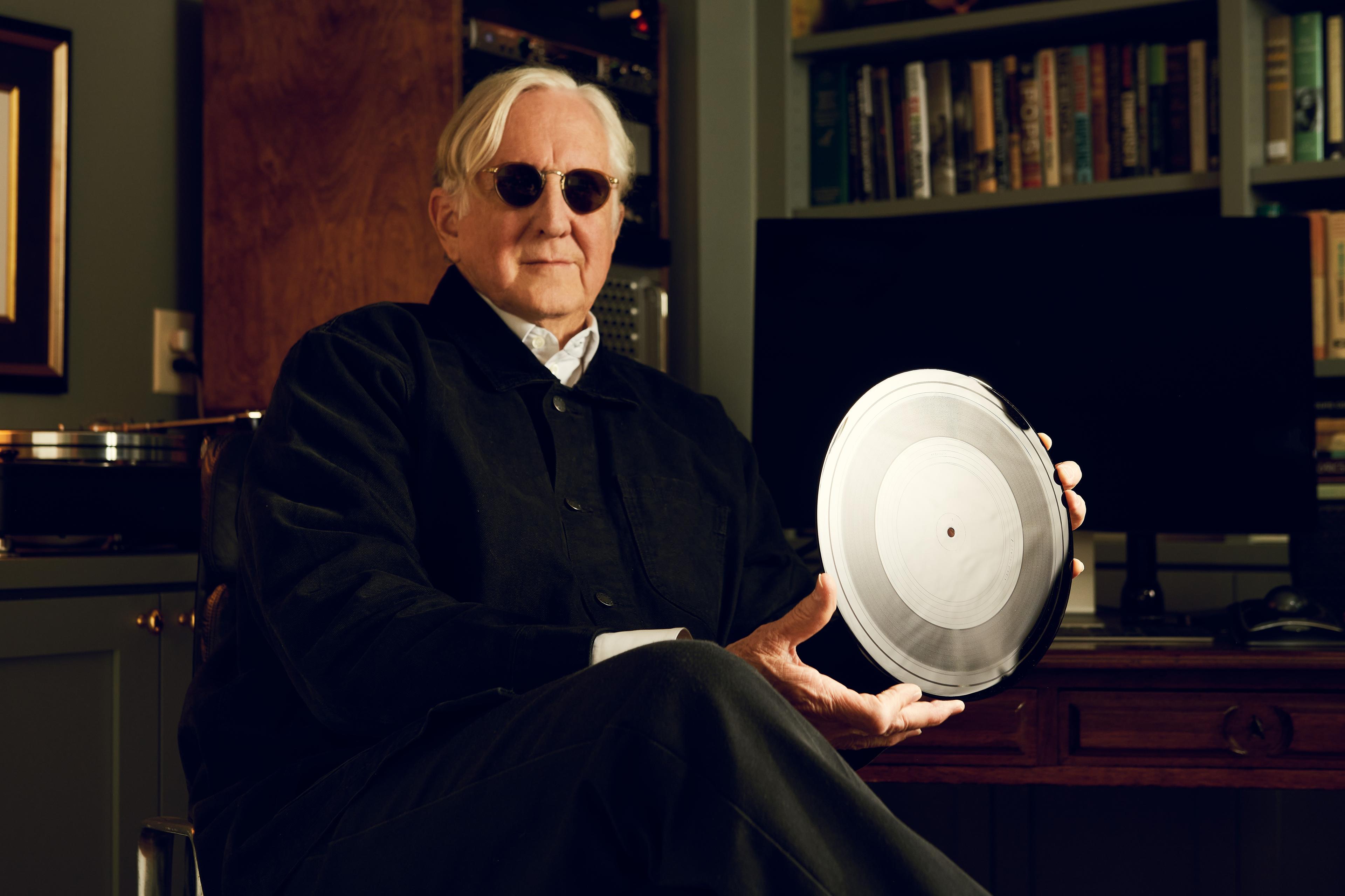 a man wearing sunglasses is sitting in a chair holding a record .