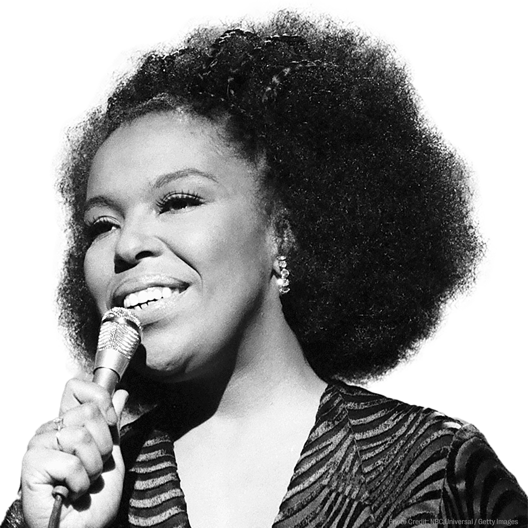 Two overlapping photos of a singer with curly hair and sunglasses at a keyboard, one in color and one in black and white, with a "Coming Soon" sticker.