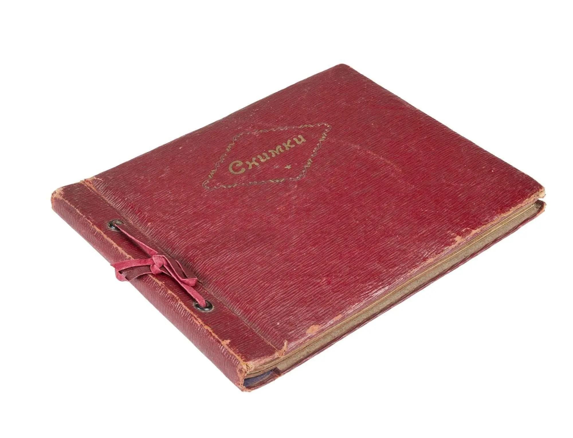 An old, worn red photo album with a ribbon binding and "Снимки" (Photos) embossed on the cover.