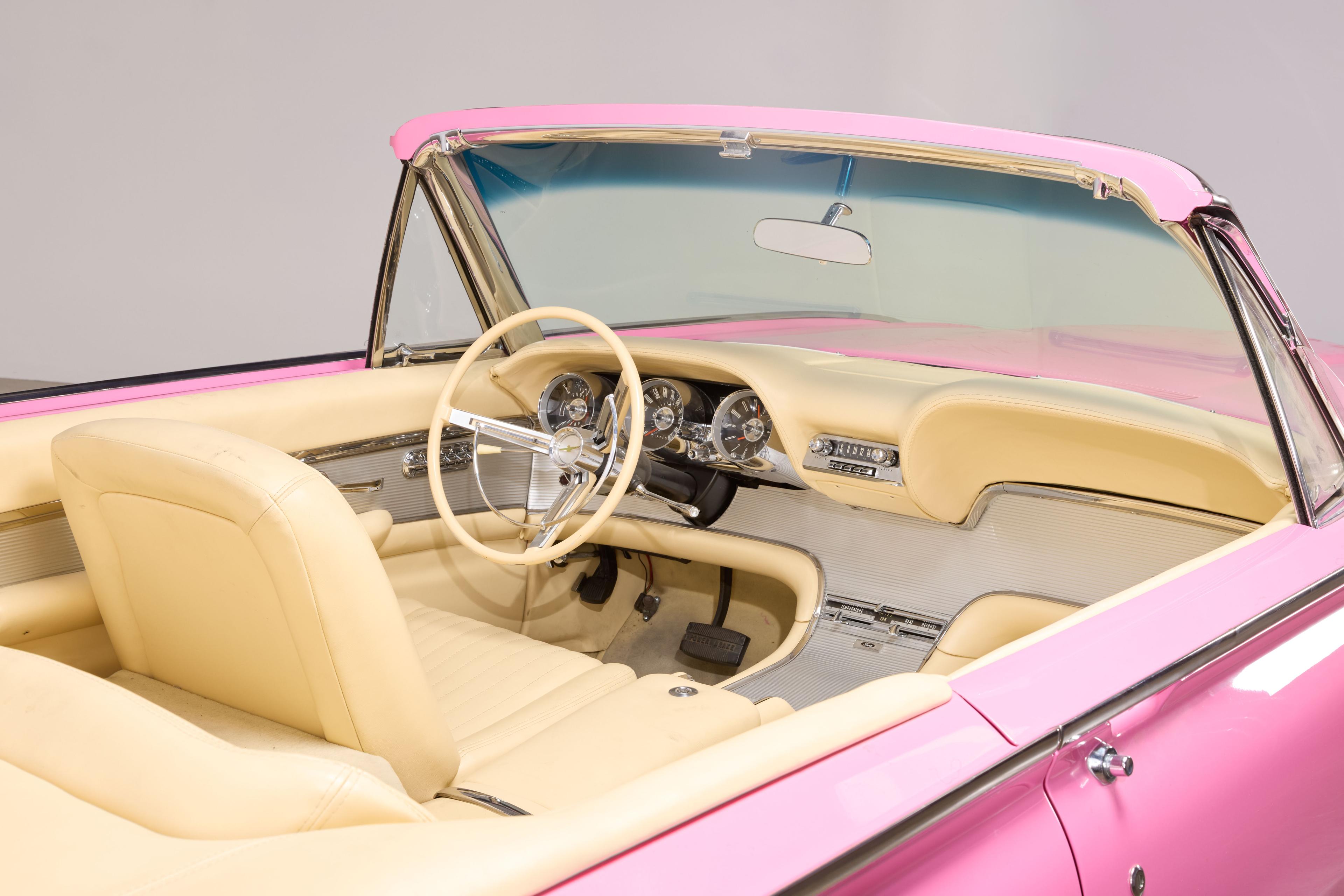 A vintage pink convertible with a cream-colored interior.
