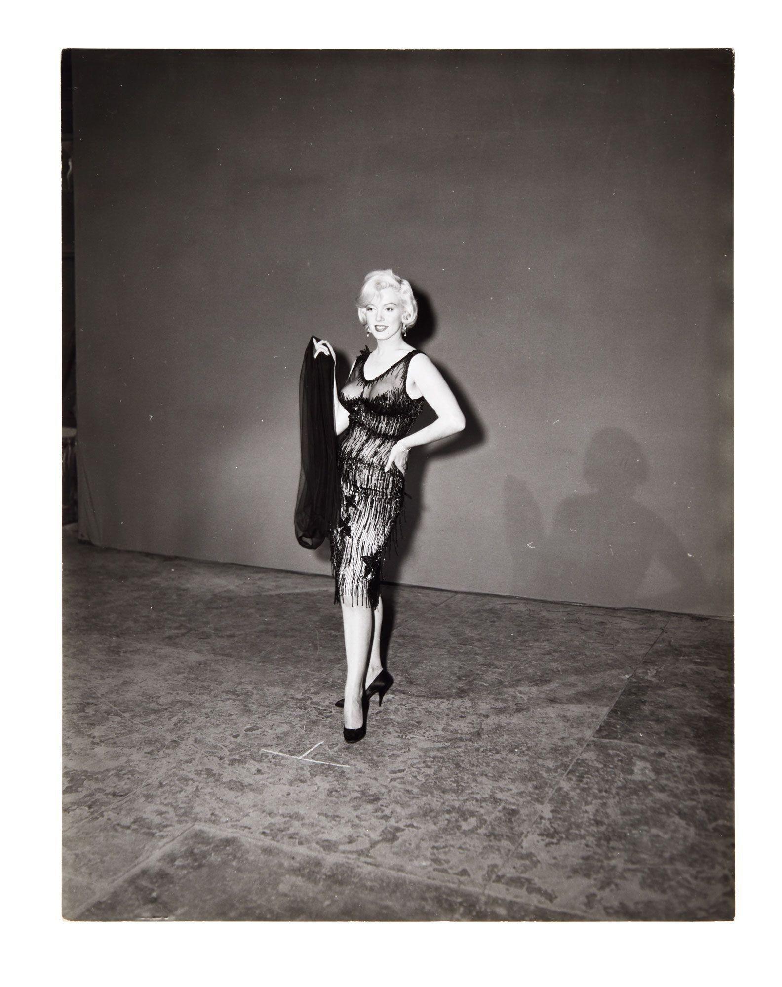 a black and white photo of a woman in a lace dress holding a scarf .