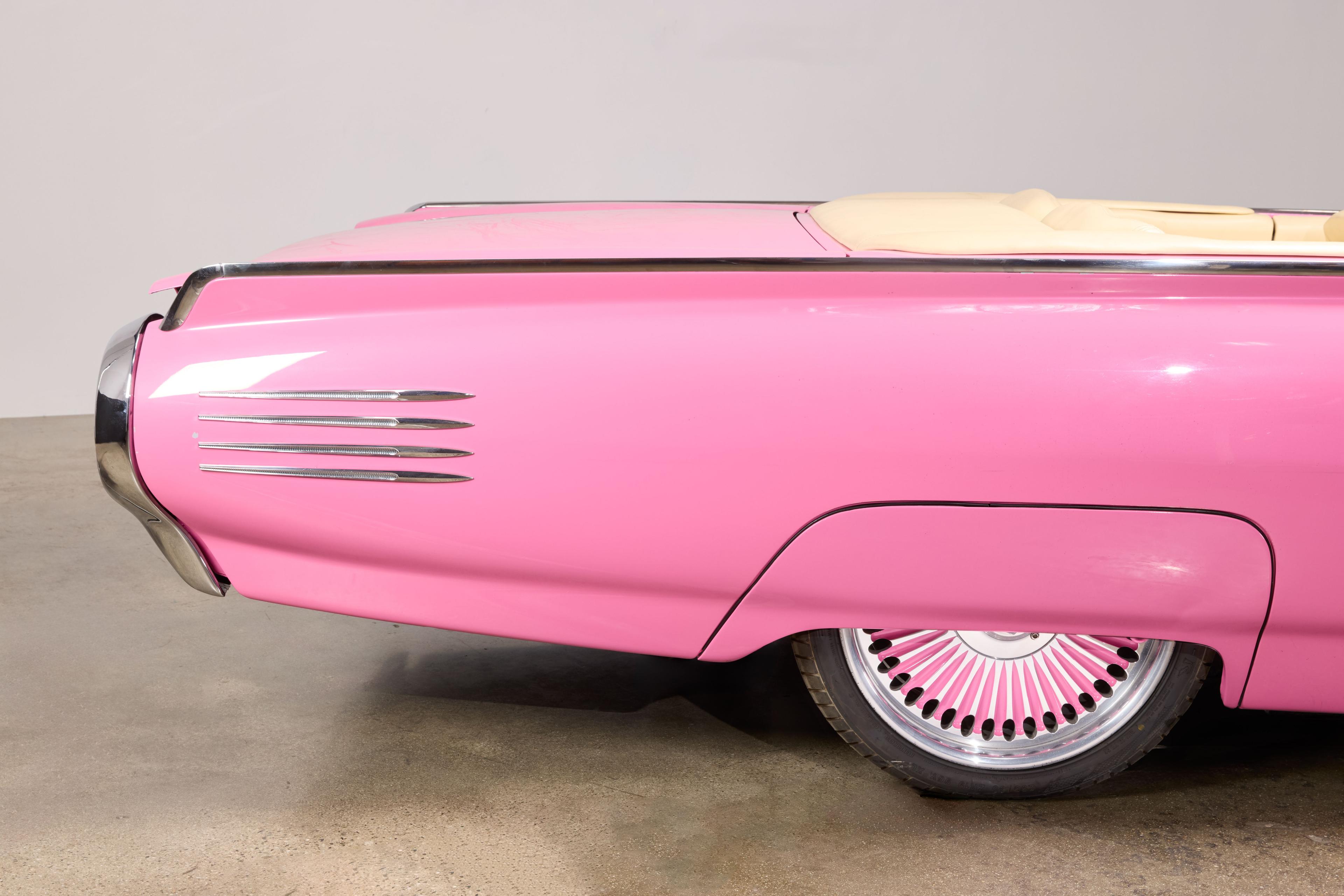Rear passenger side of a pink vintage car with chrome trim and a custom wheel with pink spokes.