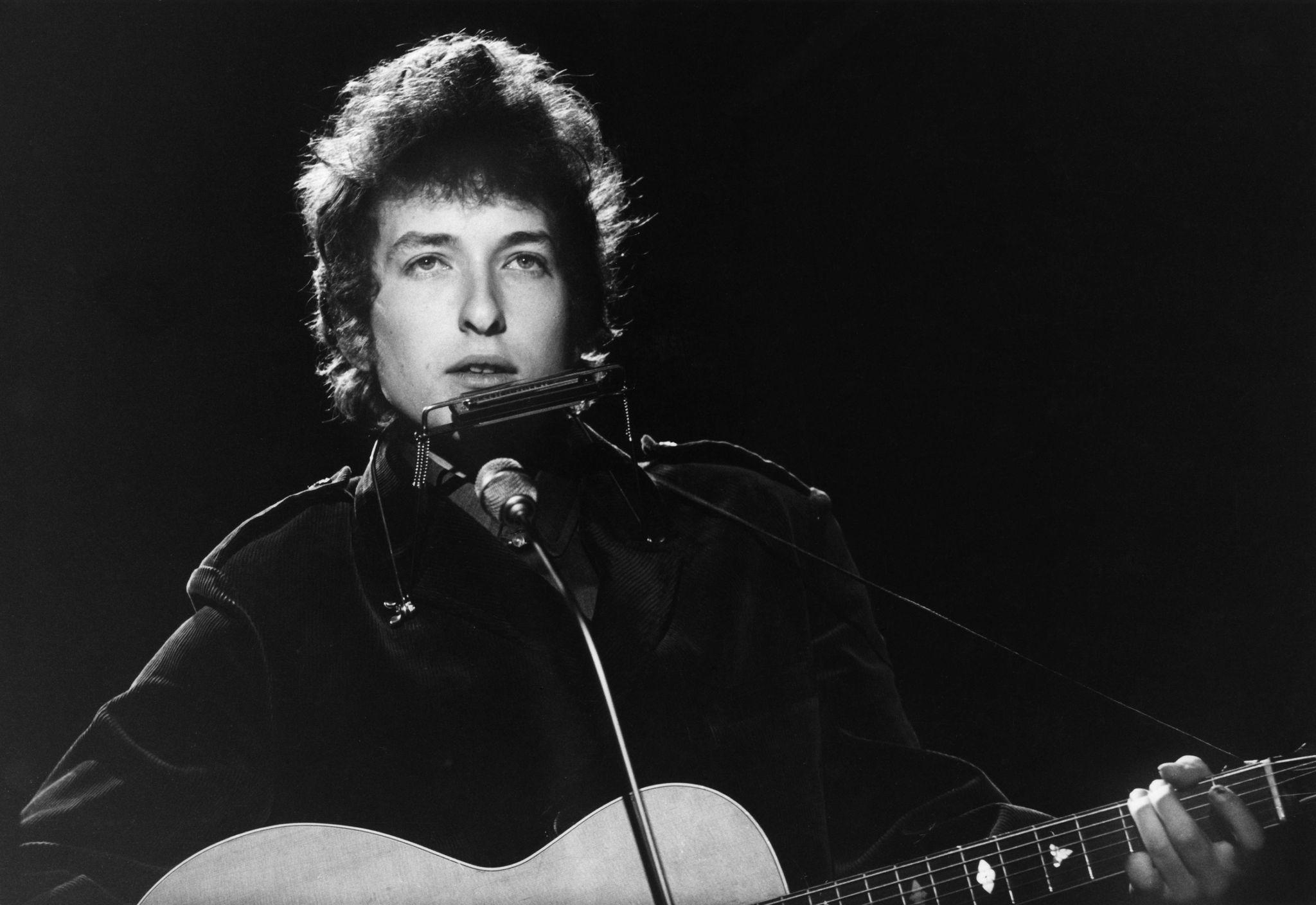 a black and white photo of a man singing into a microphone while holding a guitar .