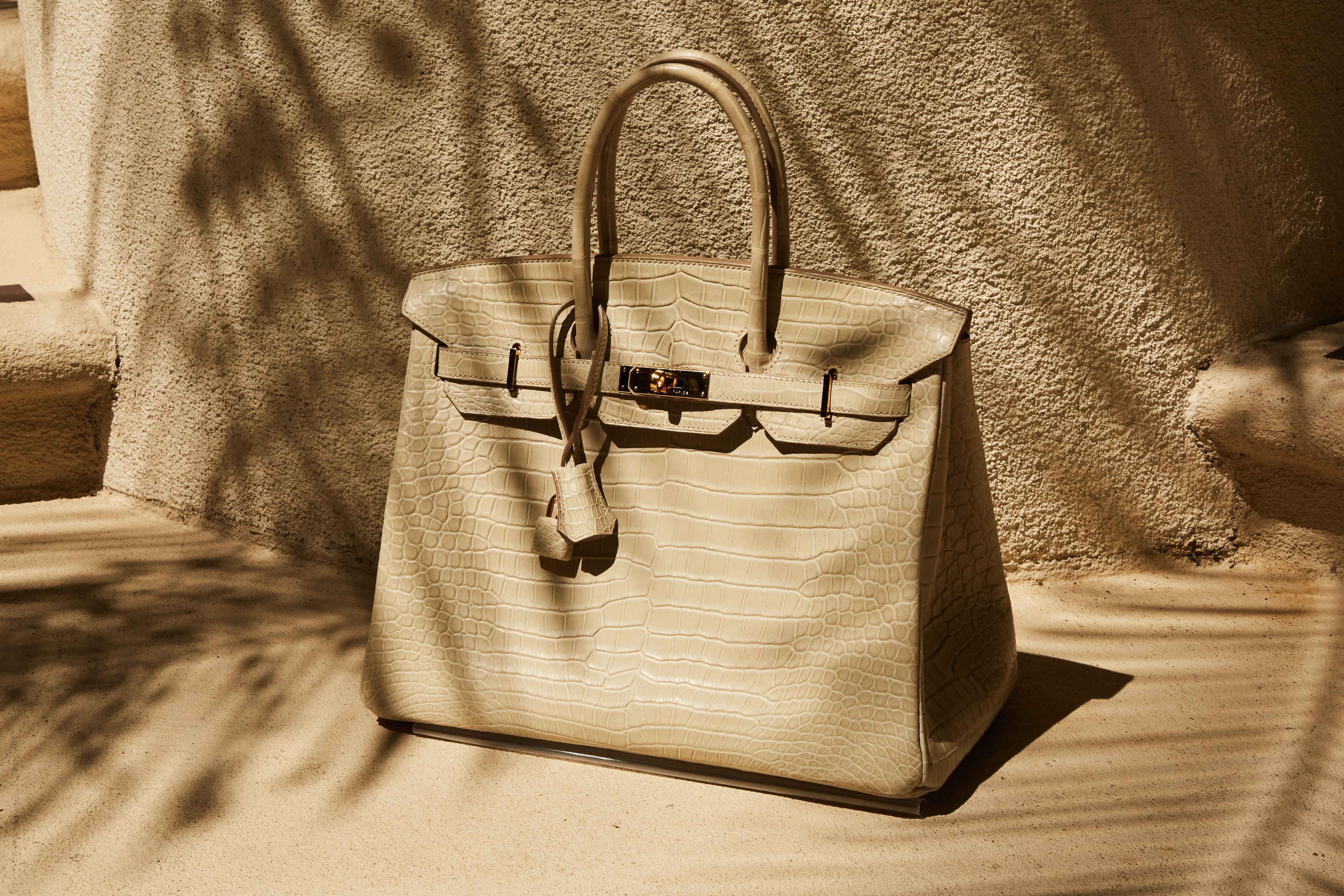 a beige hermes birkin bag is sitting on the ground in front of a wall .