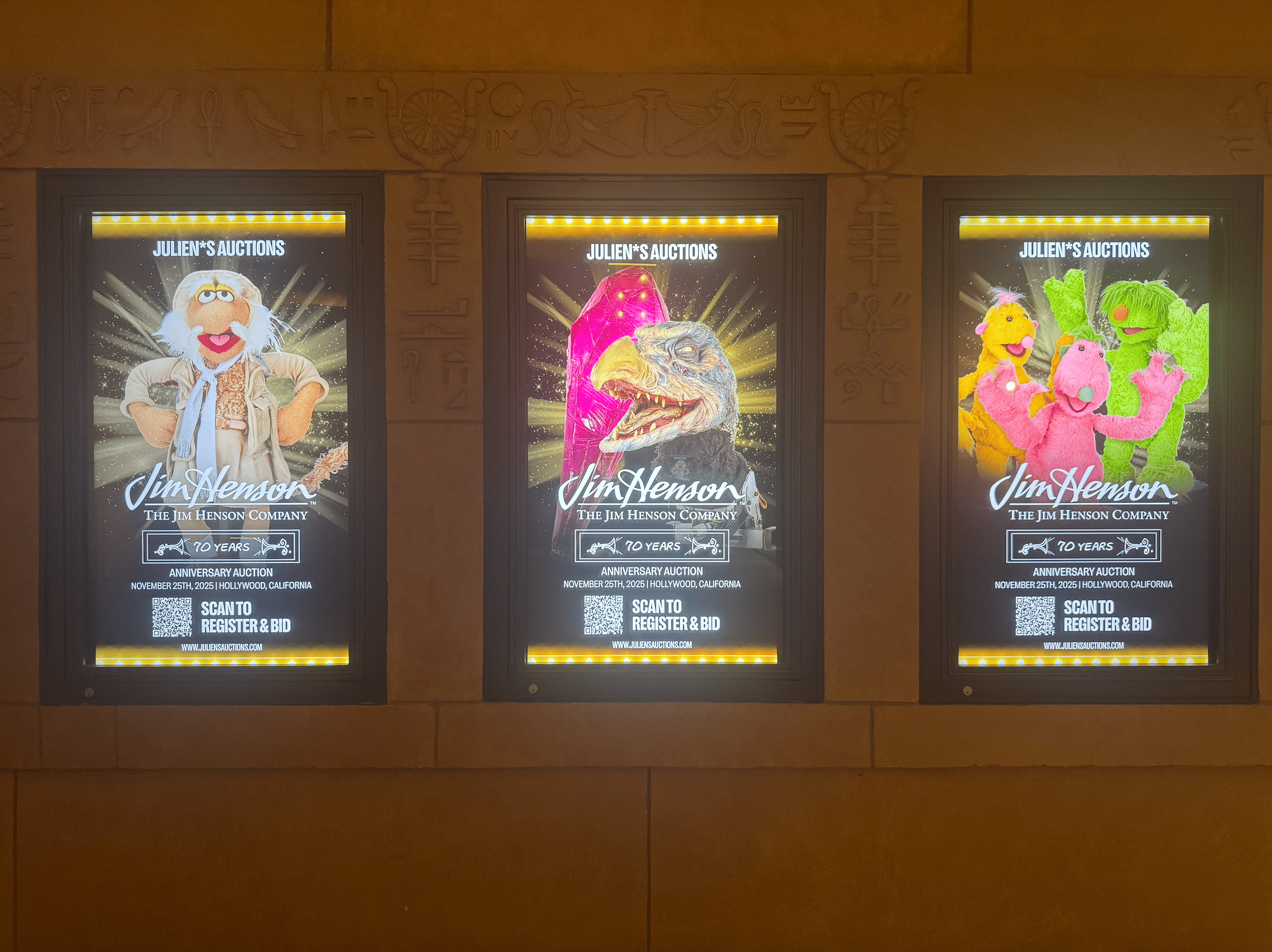 Three illuminated posters on a wall advertise "Julien's Auctions: The Jim Henson Company 70 Years," featuring various puppet characters including Dr. Bunsen Honeydew, a dinosaur, and three colorful creatures.