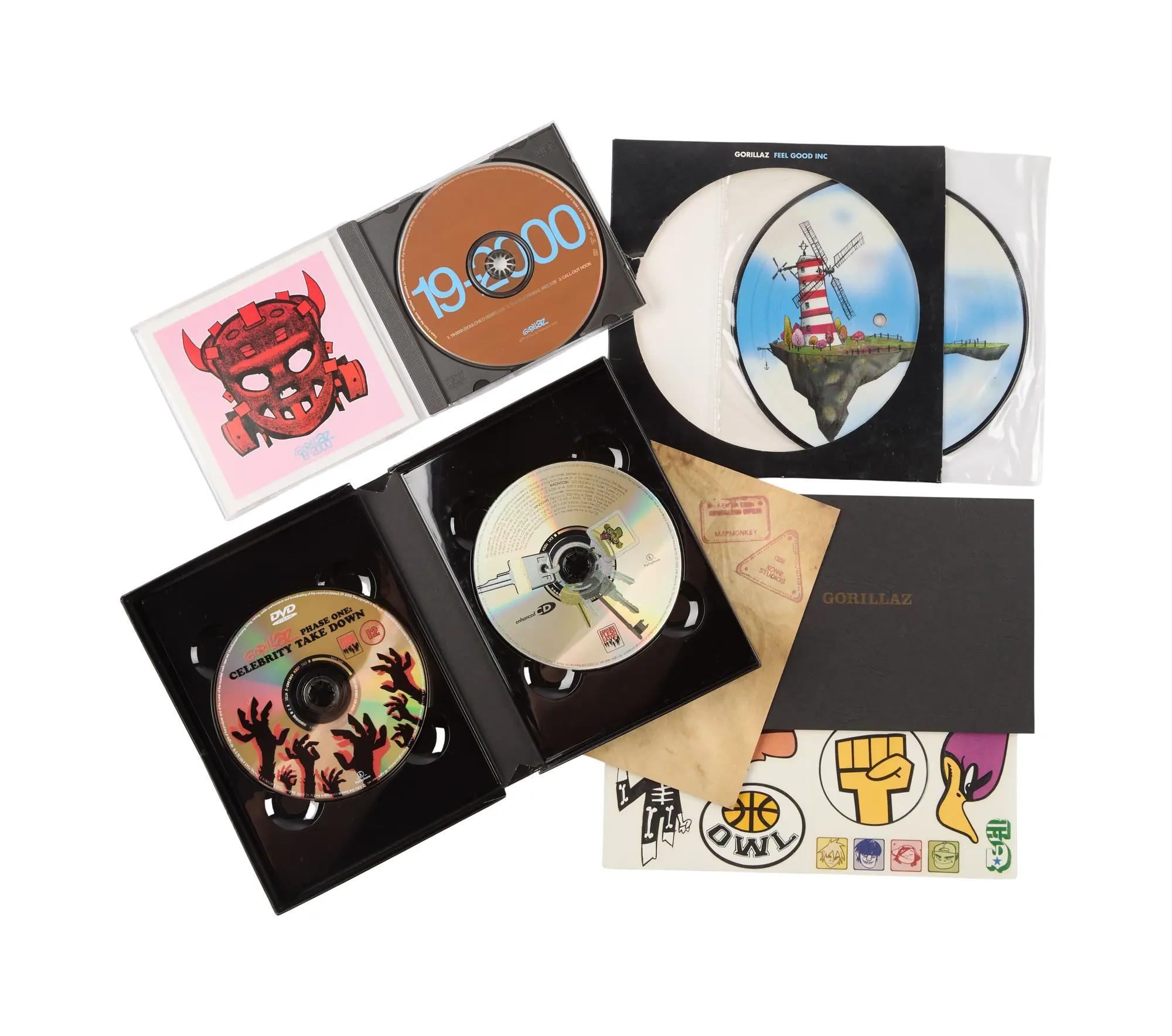 A collection of Gorillaz music and media, including CDs, DVDs, vinyl records, stickers, and a book.