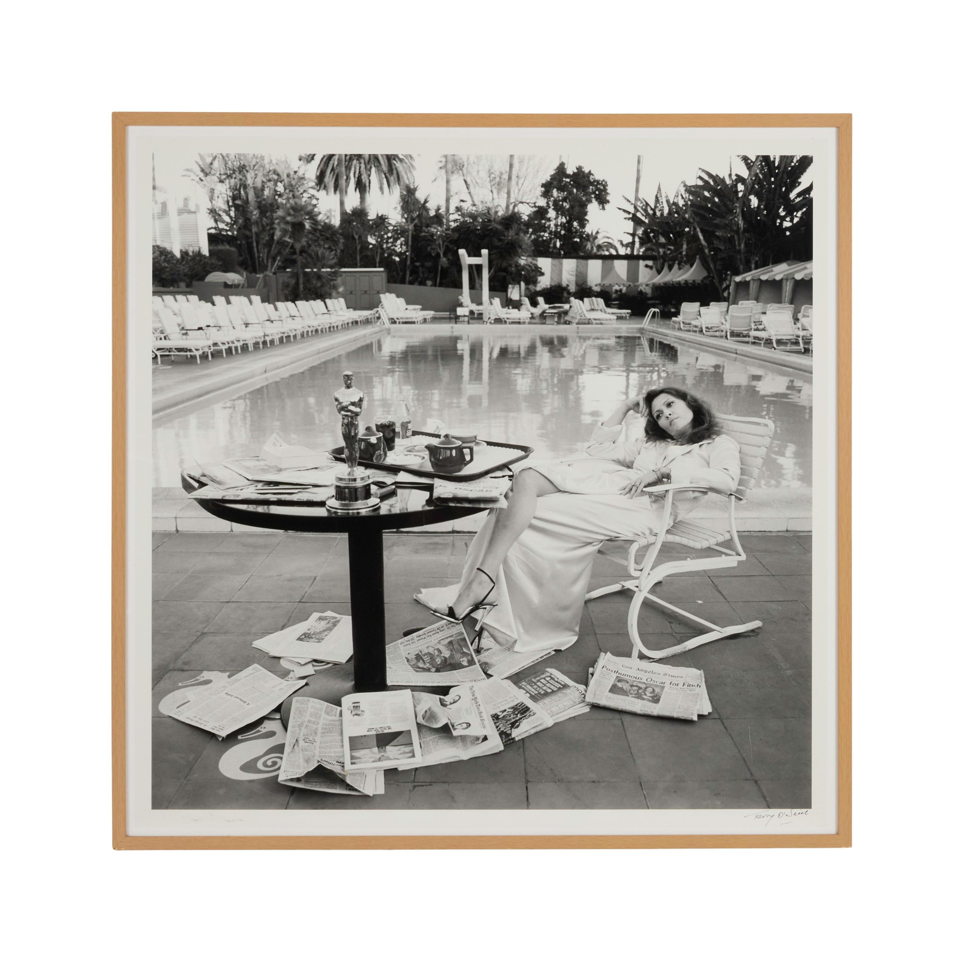Lot #99. Paul Oakenfold | "The Morning After" Photo of Faye Dunaway by Terry O'Neill a black and white photo of a woman sitting at a table by a pool .