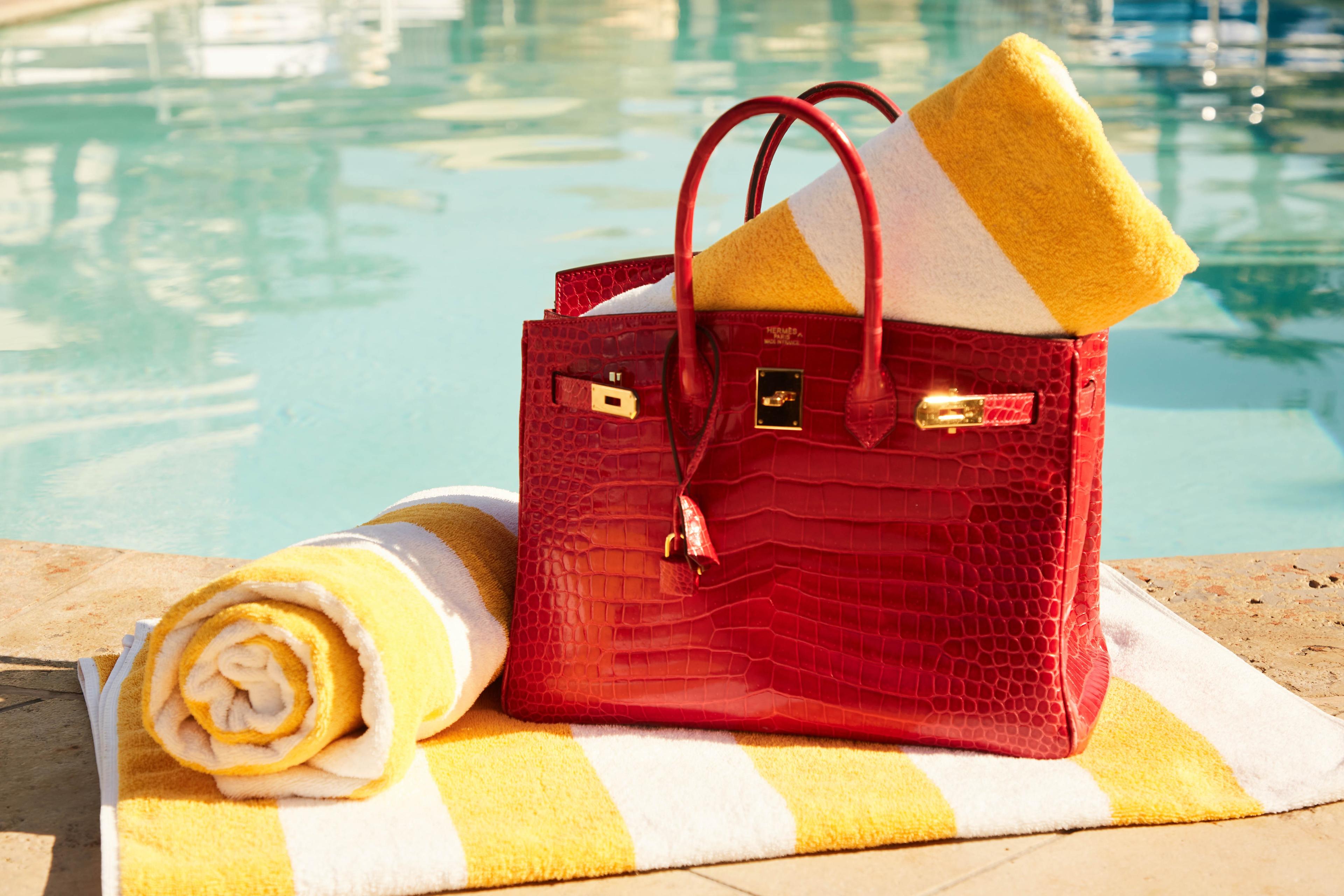 a red purse is sitting on top of a yellow and white striped towel next to a pool .