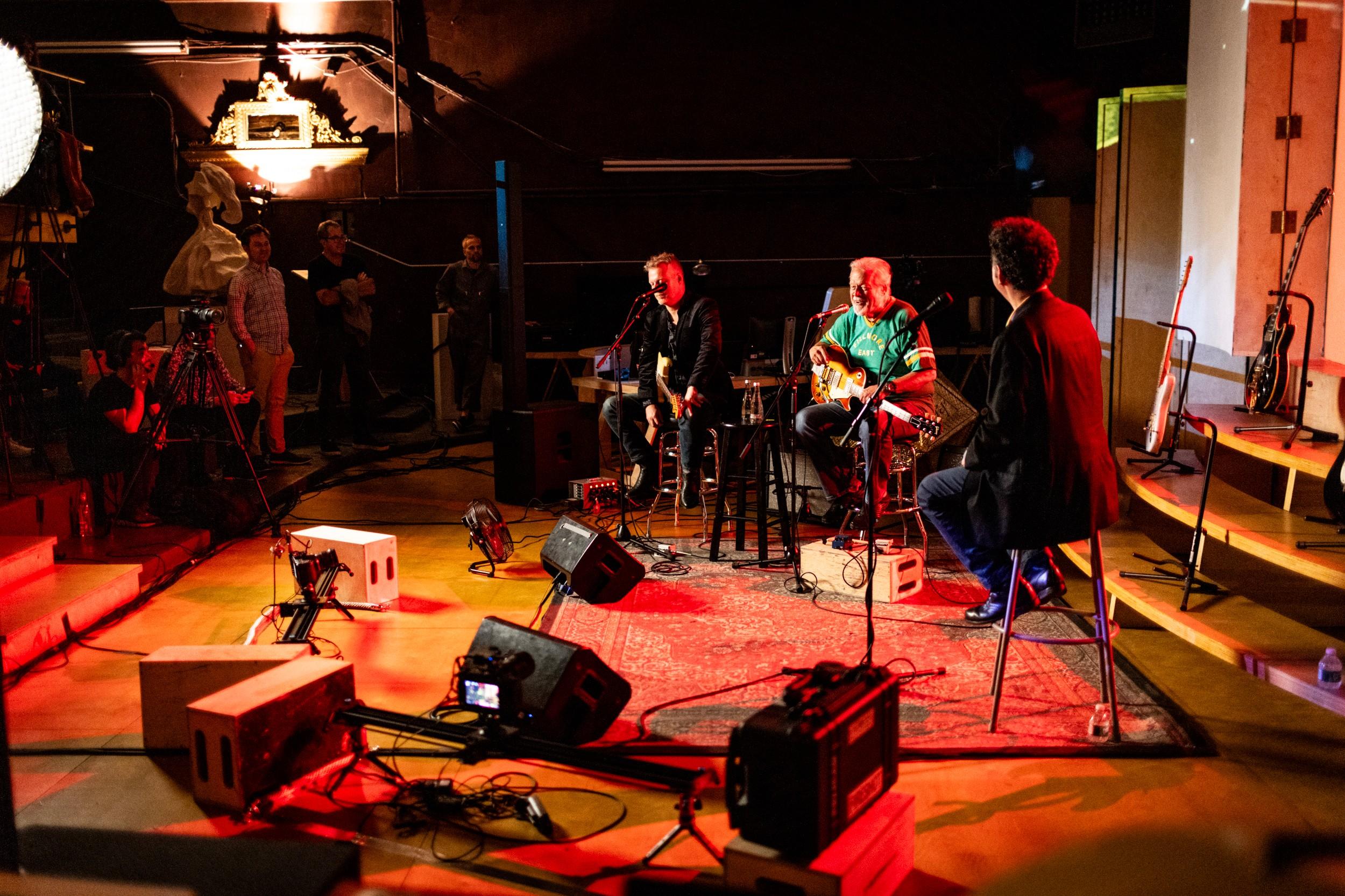 a group of men are sitting on stools on a stage playing guitars .