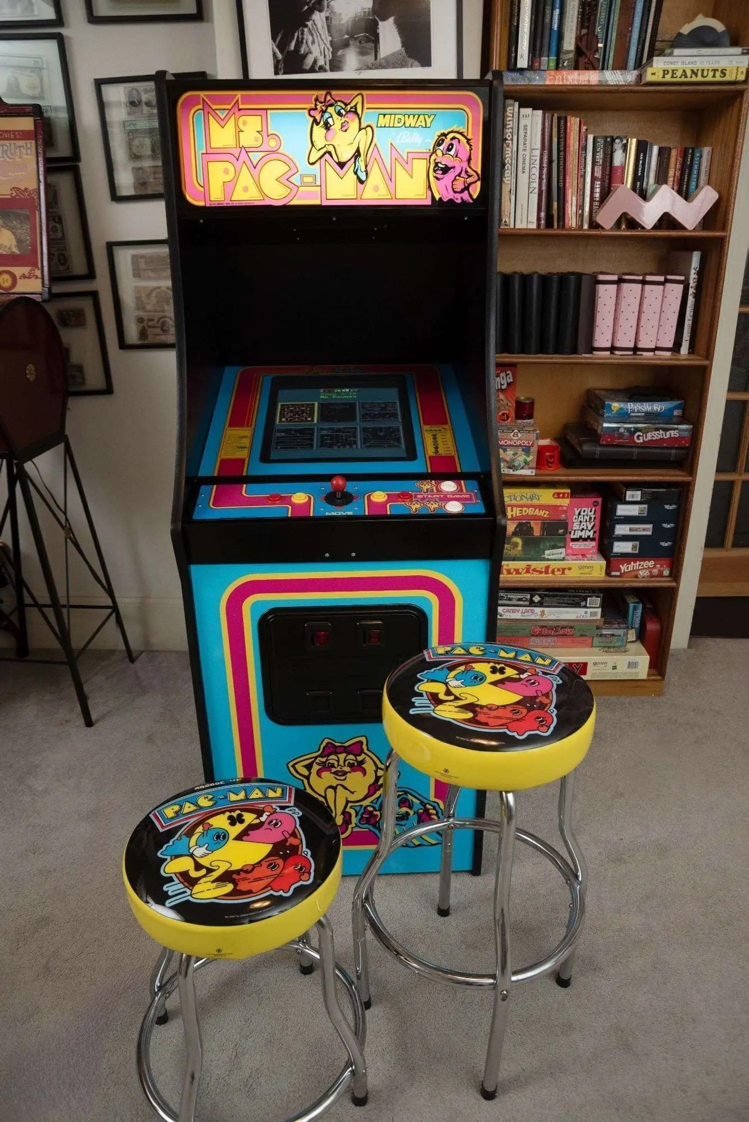 A bright blue Ms. Pac-Man arcade game cabinet with yellow and pink trim, featuring two matching yellow Pac-Man bar stools.