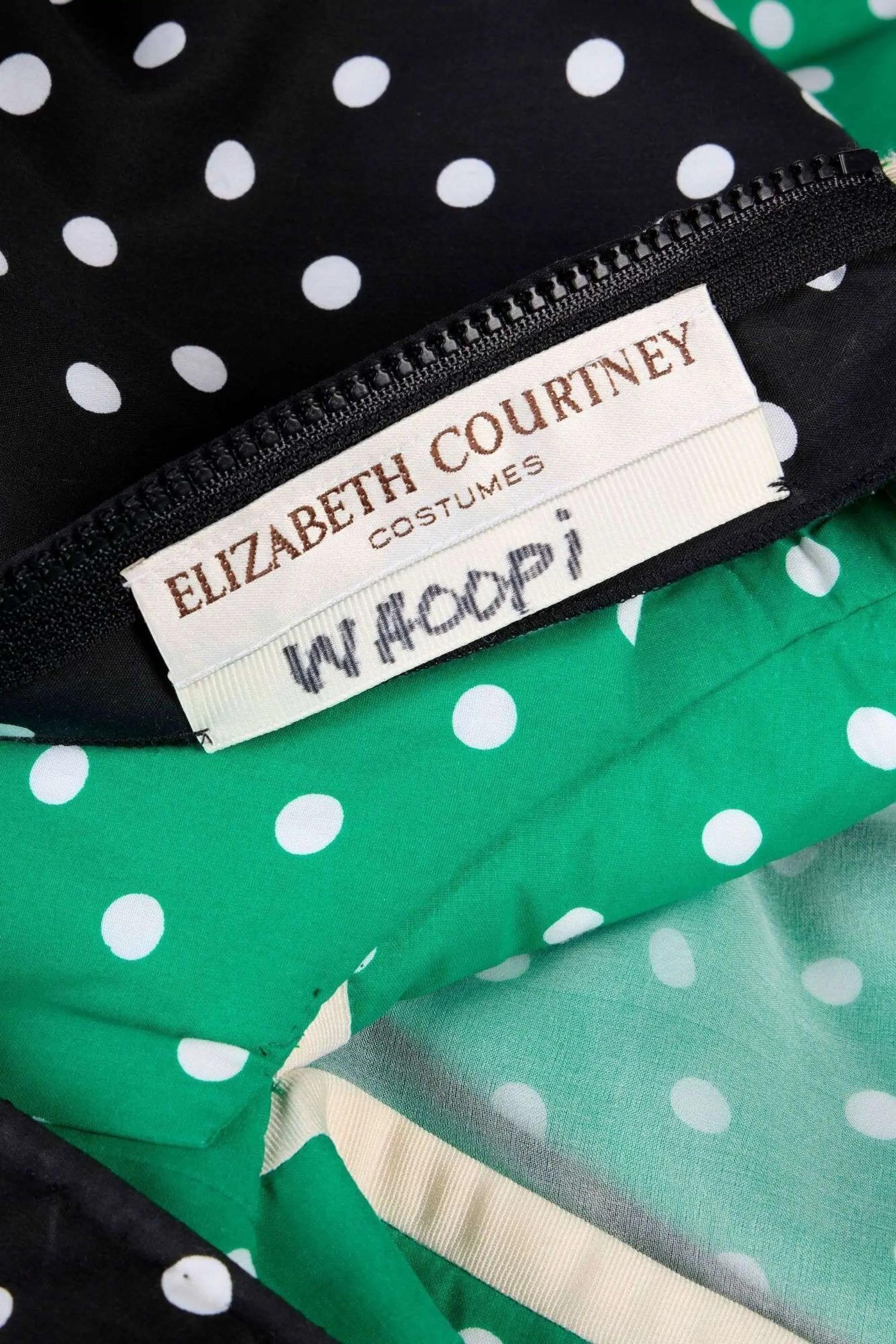 Close-up of a black and green polka dot garment with a zipper and a white label reading "ELIZABETH COURTNEY COSTUMES WHOOPI".