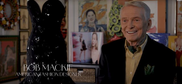 bob mackie american fashion designer is smiling in front of a black dress