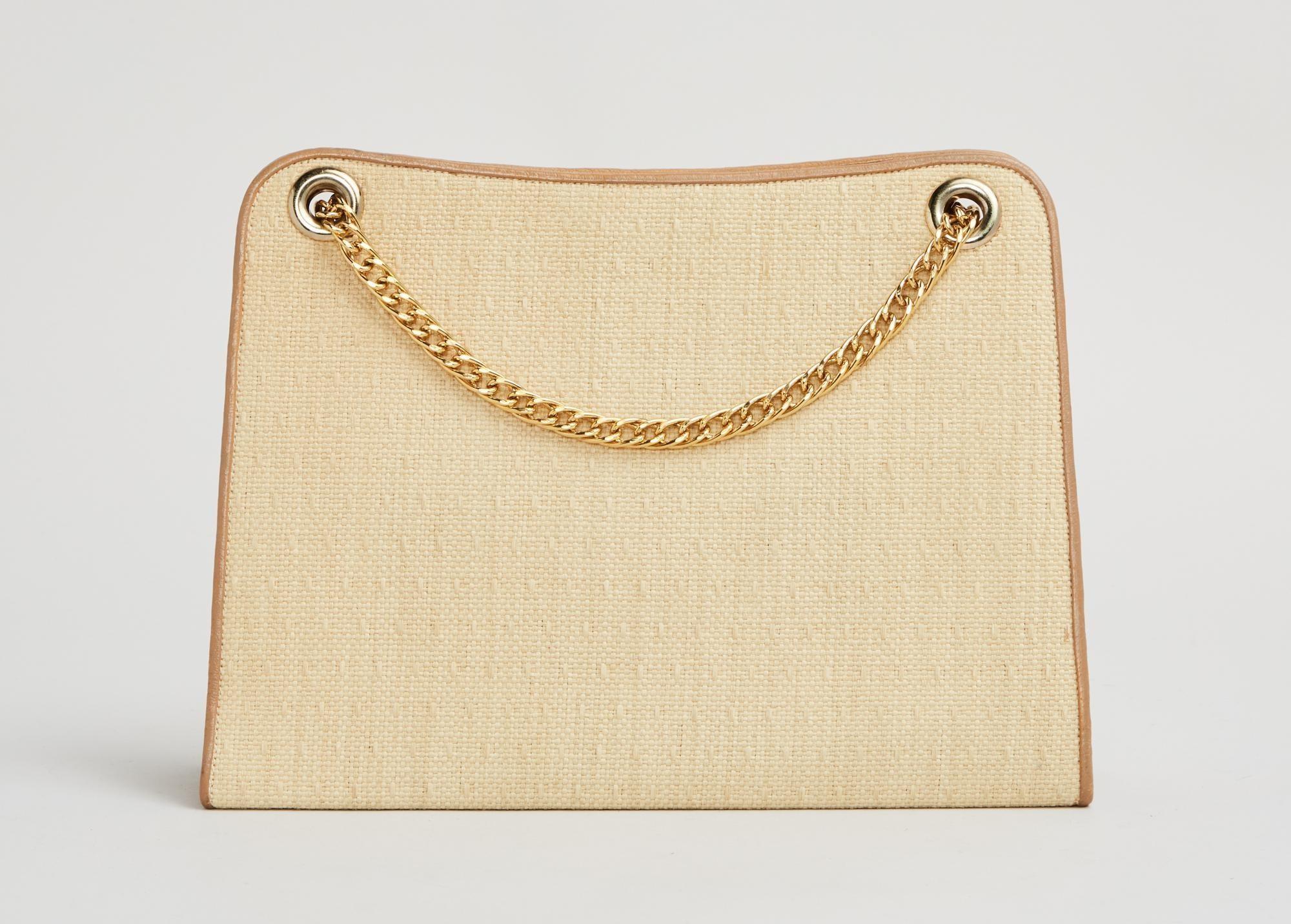 Lot #30. Elizabeth Taylor | 1964 Cartier Yellow Straw Shoulder Bag a beige purse with a gold chain on a white background .