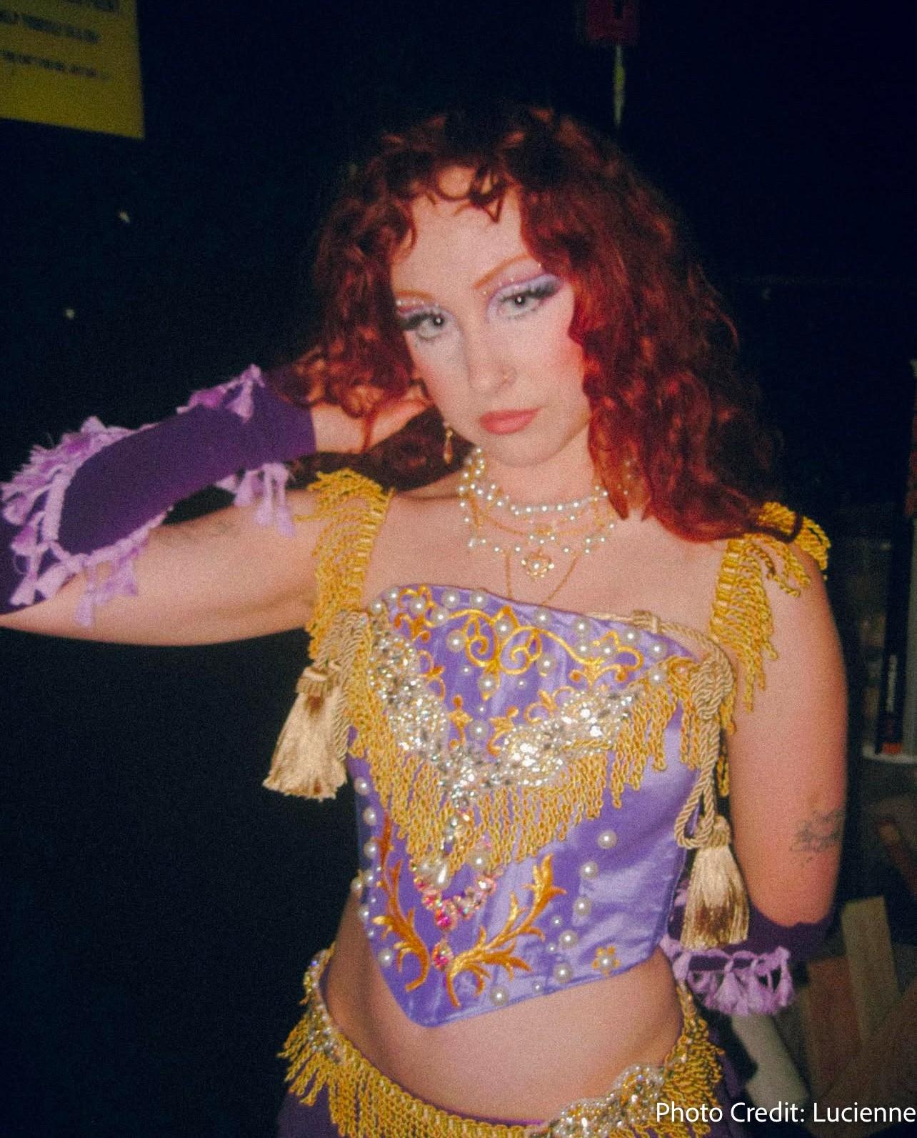 a woman with red hair is wearing a purple and gold outfit