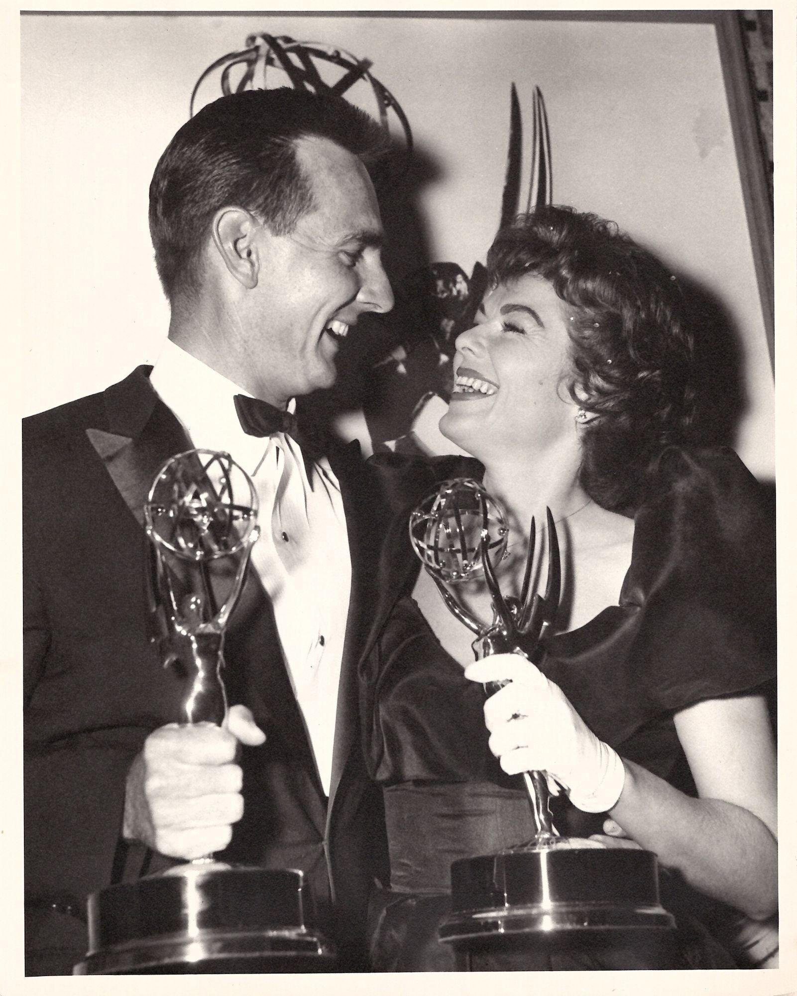 a black and white photo of a man and woman holding emmy trophies