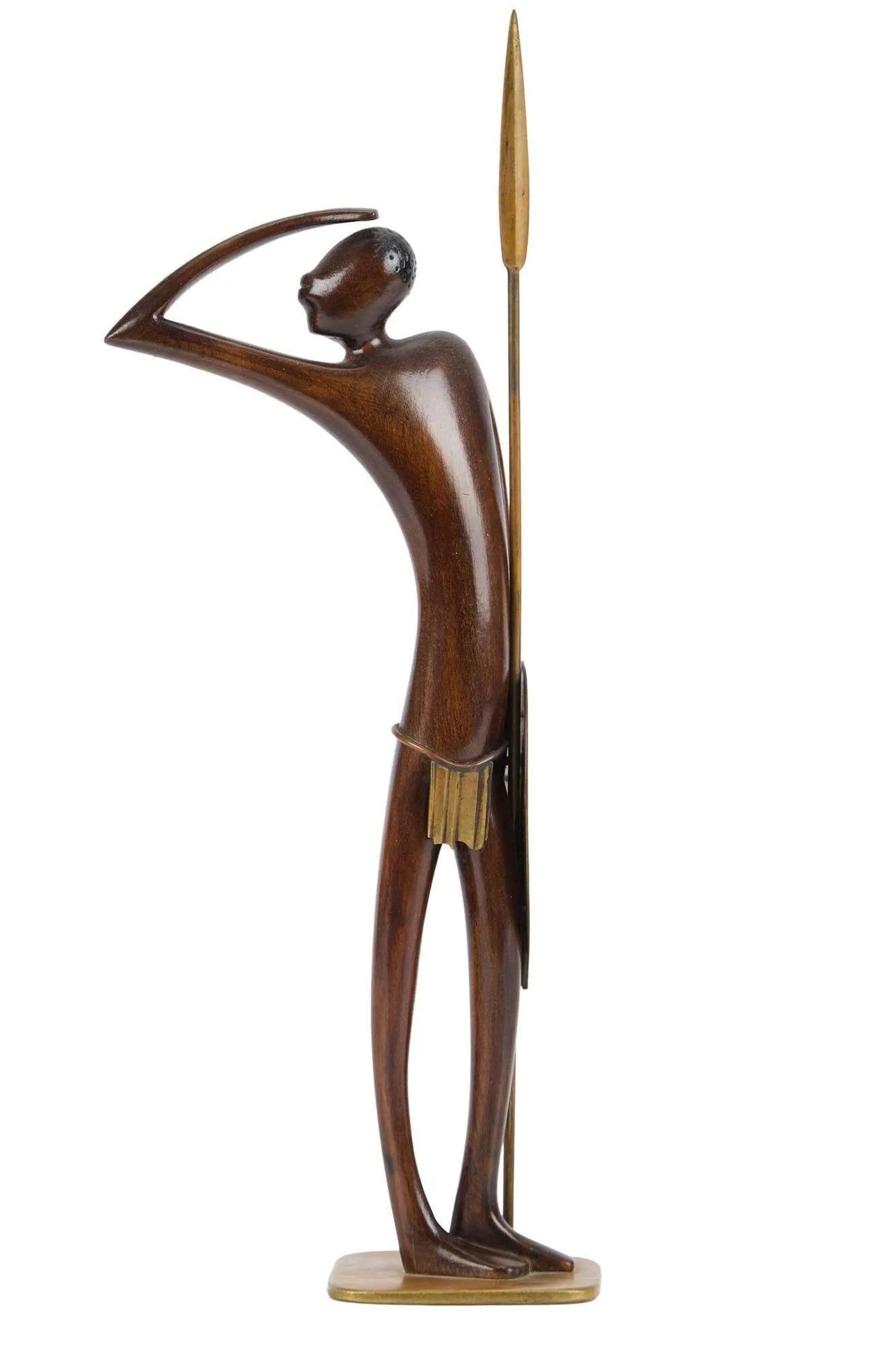 Lot #375. Whoopi Goldberg | Hagenauer Werkstatte Bronze Male Warrior Stylized dark wood sculpture of a man shading his eyes, holding a spear with brass accents.
