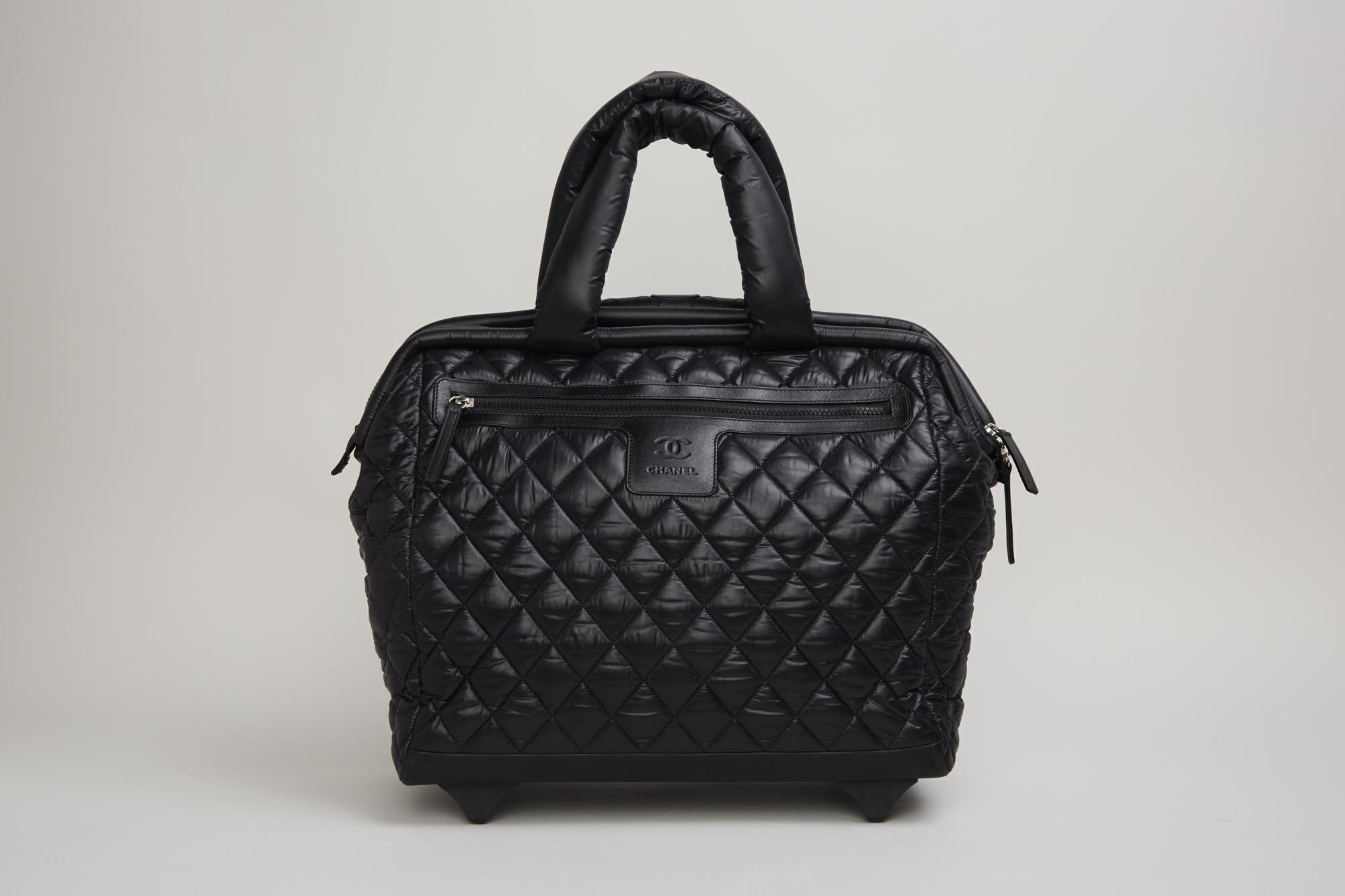 a black quilted bag with wheels and a handle on a white background .