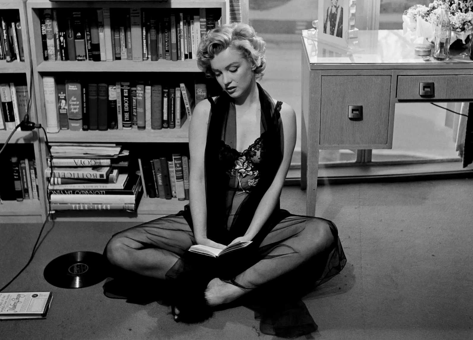 a black and white image of actress marilyn monroe sitting on a floor reading a book