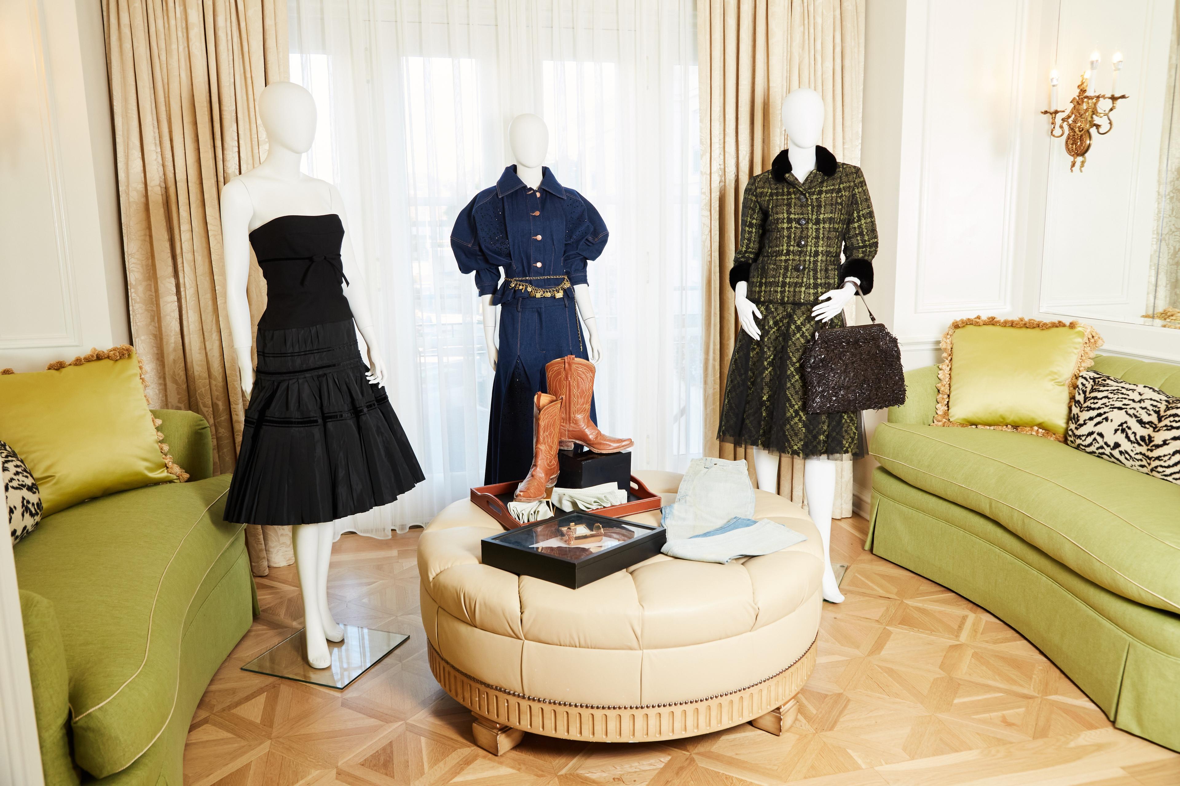 a living room with a couch , ottoman , and mannequins wearing dresses .