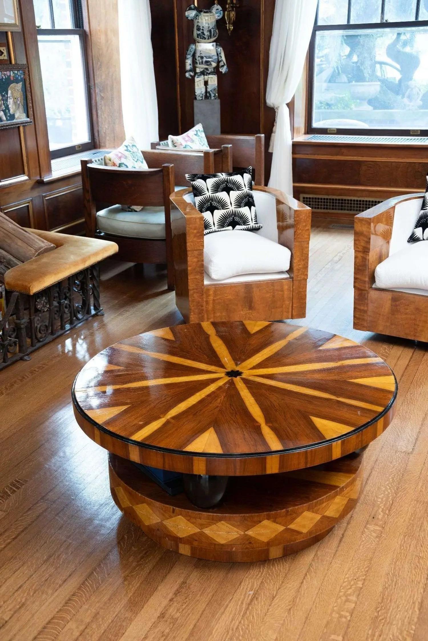 A room with a round wooden coffee table featuring a starburst pattern, modern wooden armchairs with white cushions, and a large bear figurine.