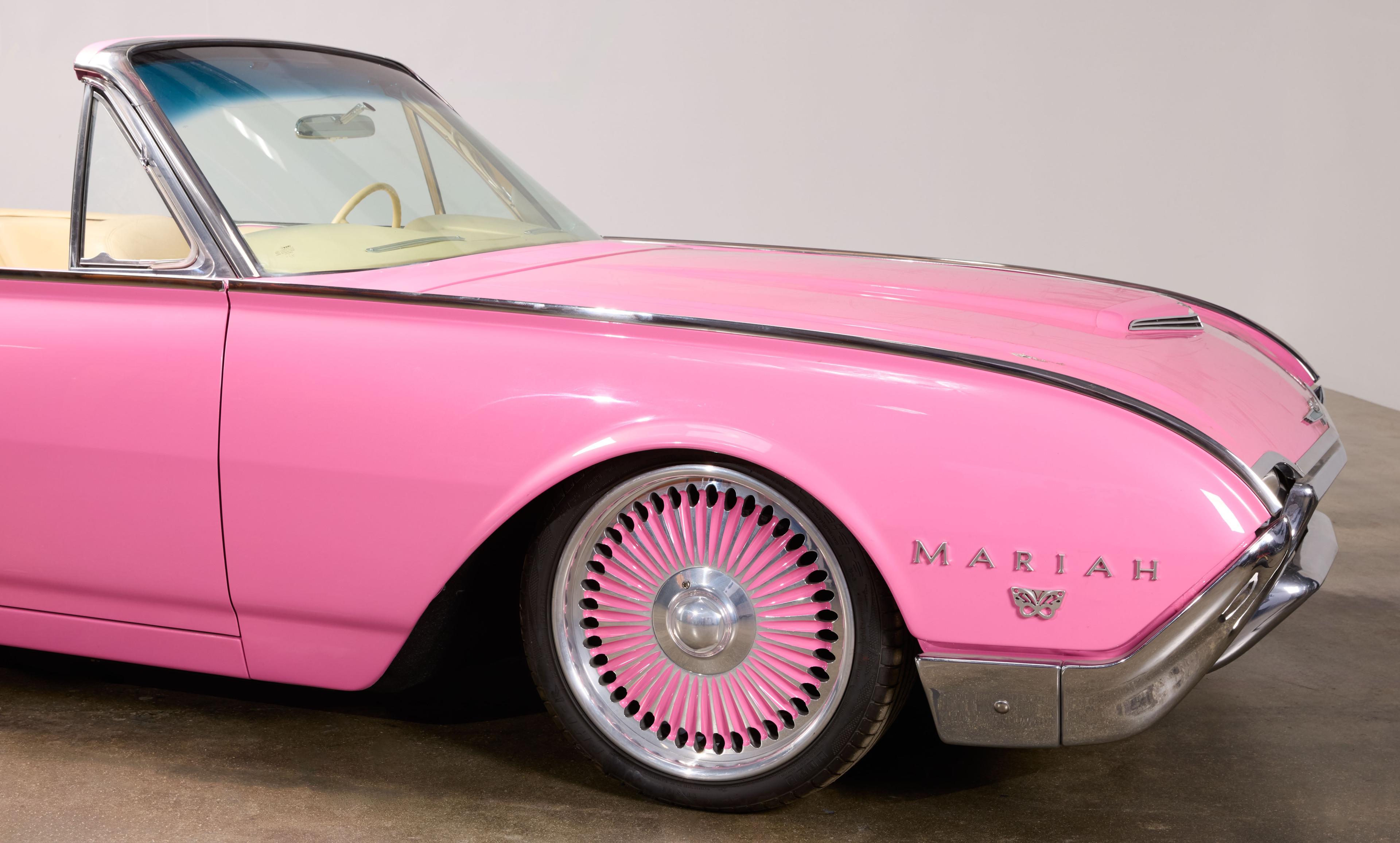 Pink classic convertible car with custom pink spoke wheels and "MARIAH" emblem on the fender.